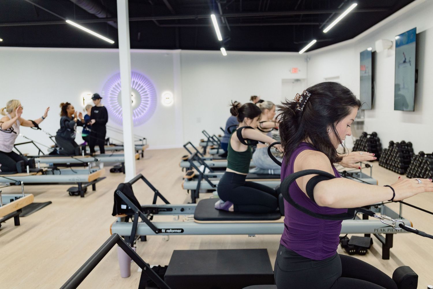People exercising on pilates reformer machines during a fitness class in a bright studio space.