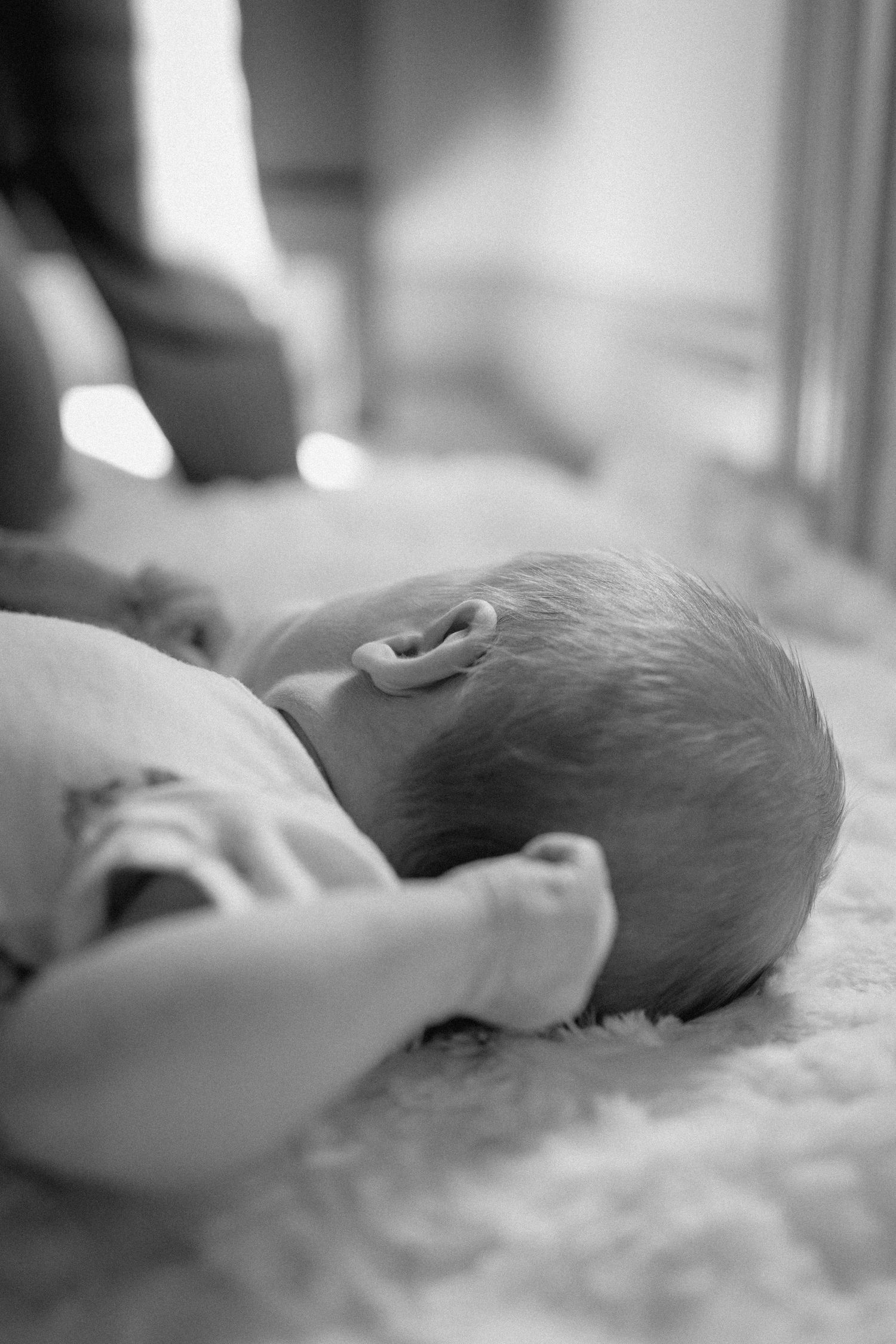 Black and white photo series showing a gentle hand caressing a sleeping newborn baby's head on soft blanket.