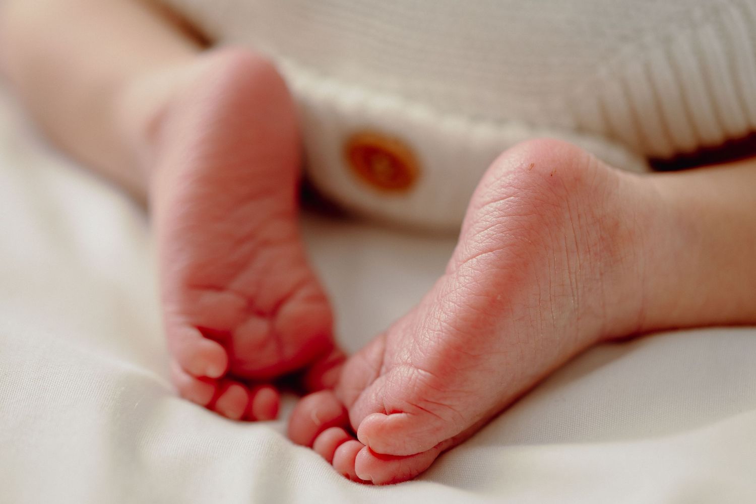 Close-up of tiny newborn baby feet resting on soft white fabric.