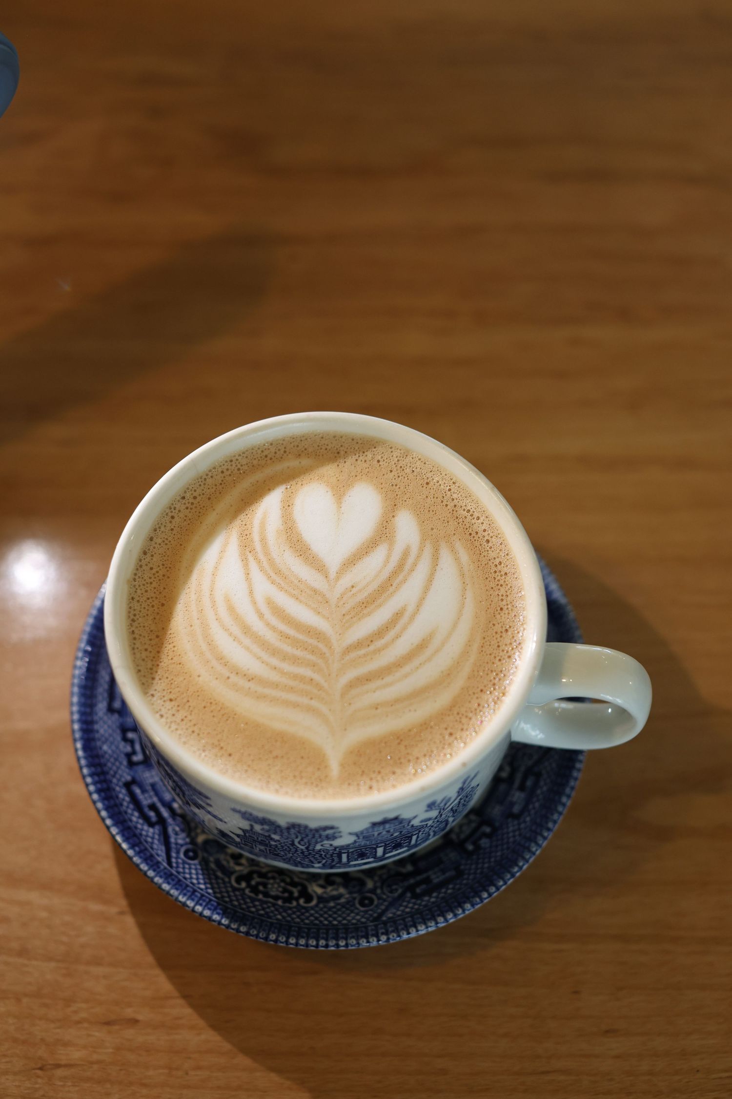 A latte art heart design in creamy foam sits atop an espresso drink served in a blue and white patterned saucer.