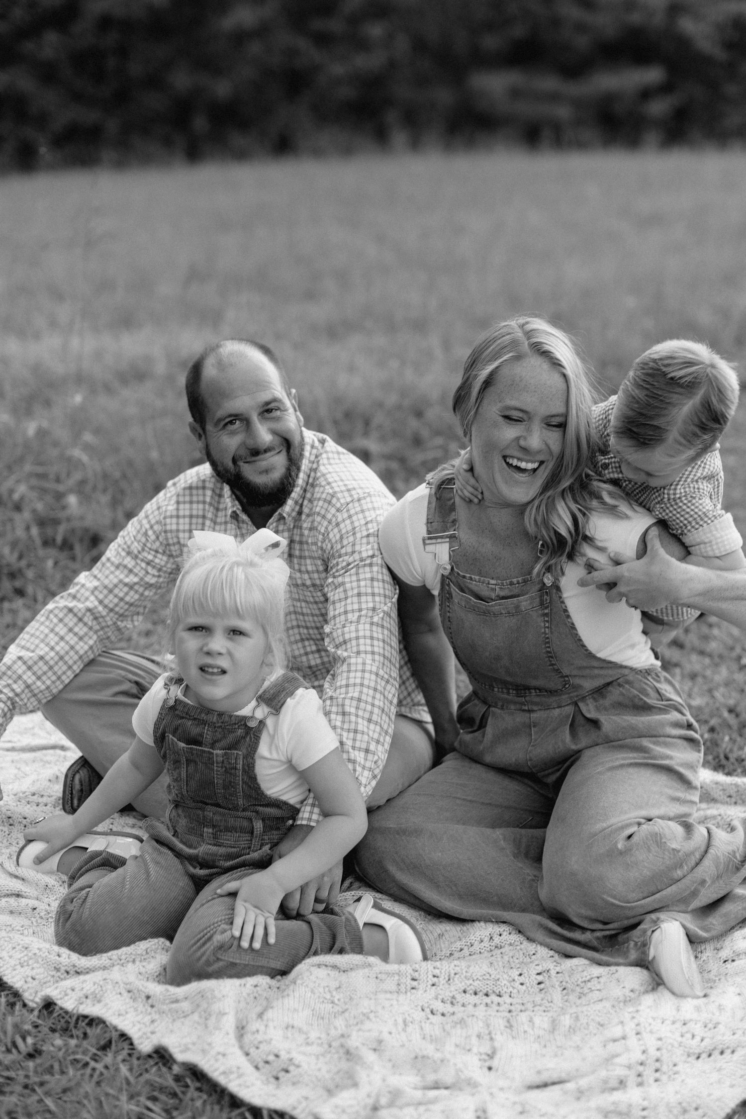 A black and white photo series of a family having fun and playing together while sitting on a blanket outdoors.