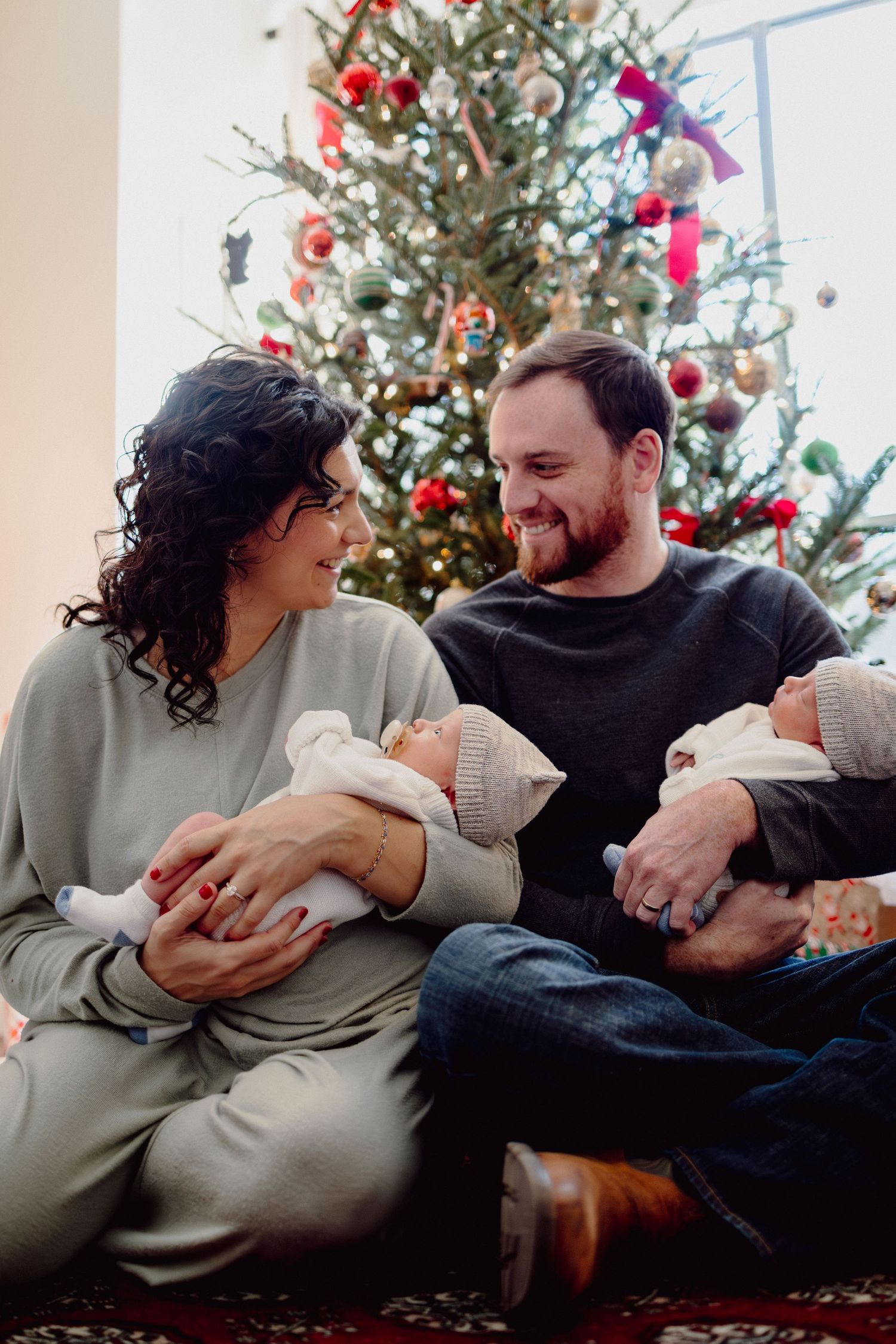A couple relaxes on the floor in front of a decorated Christmas tree during the holiday season.