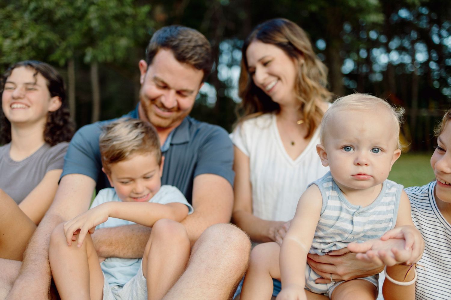 A group of families sitting together outdoors on a sunny day enjoying a casual gathering.
