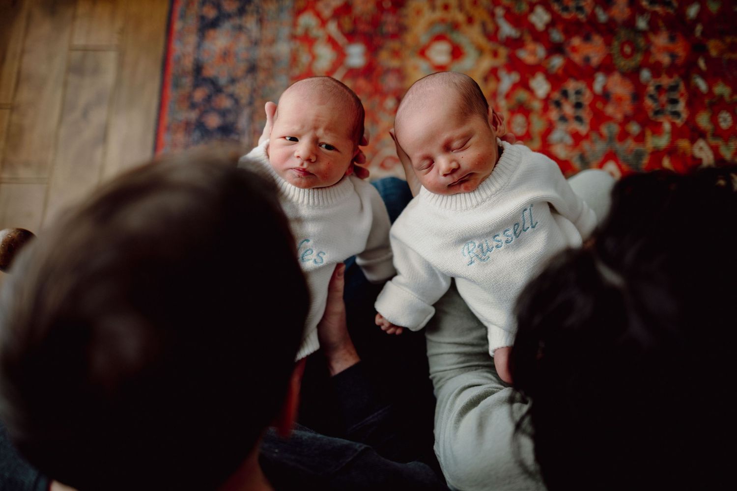 Two infants in white clothing lay side by side on a floral patterned surface.