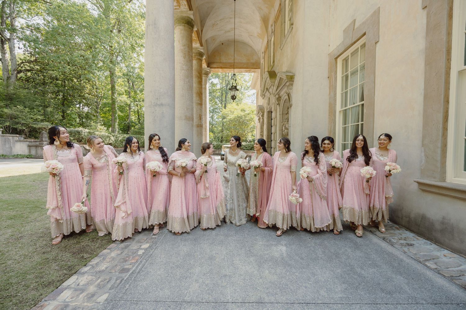 Bridesmaids in pink dresses lined up against stone building exterior.