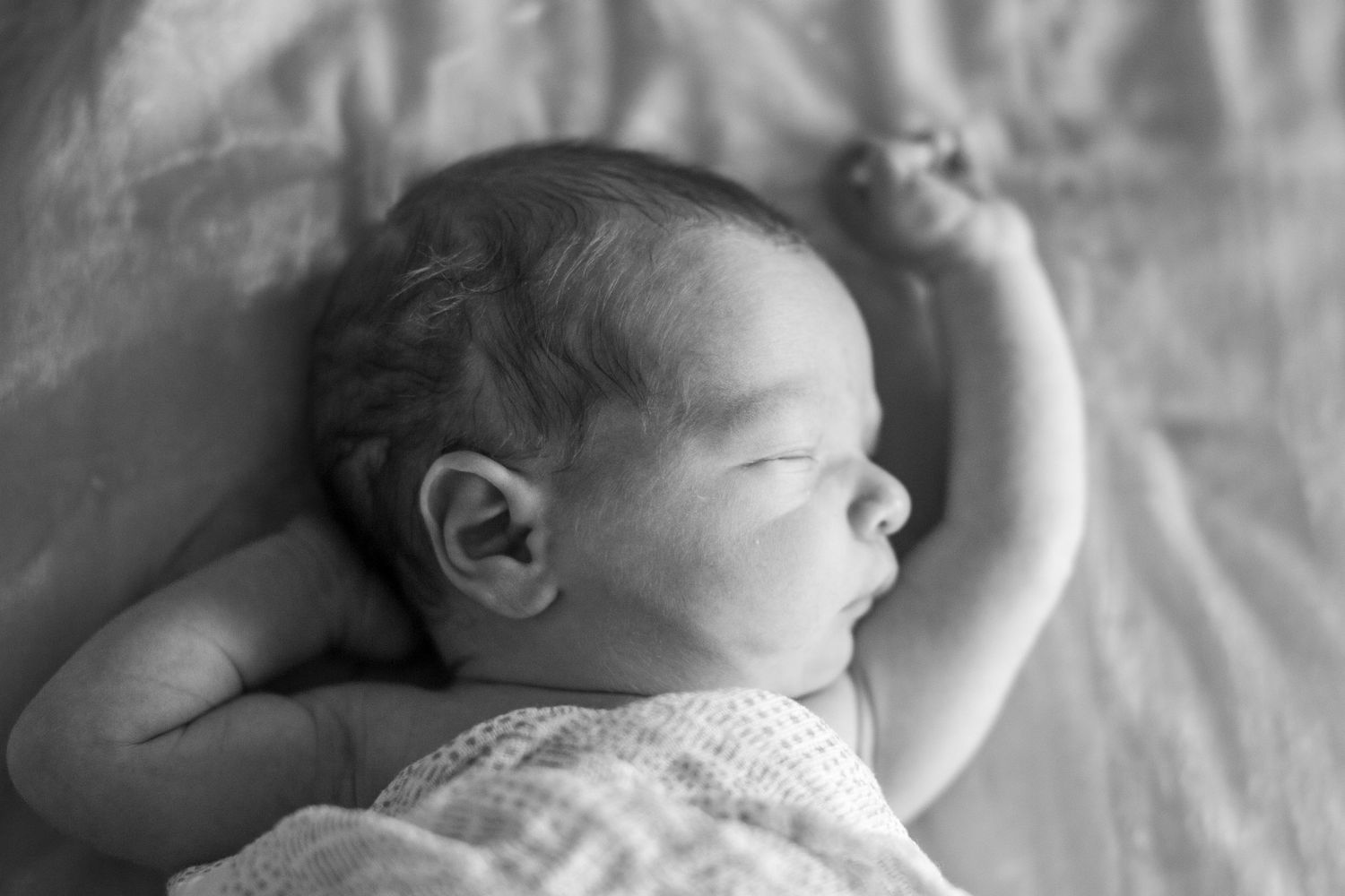 Black and white image of sleeping newborn on soft bedding.