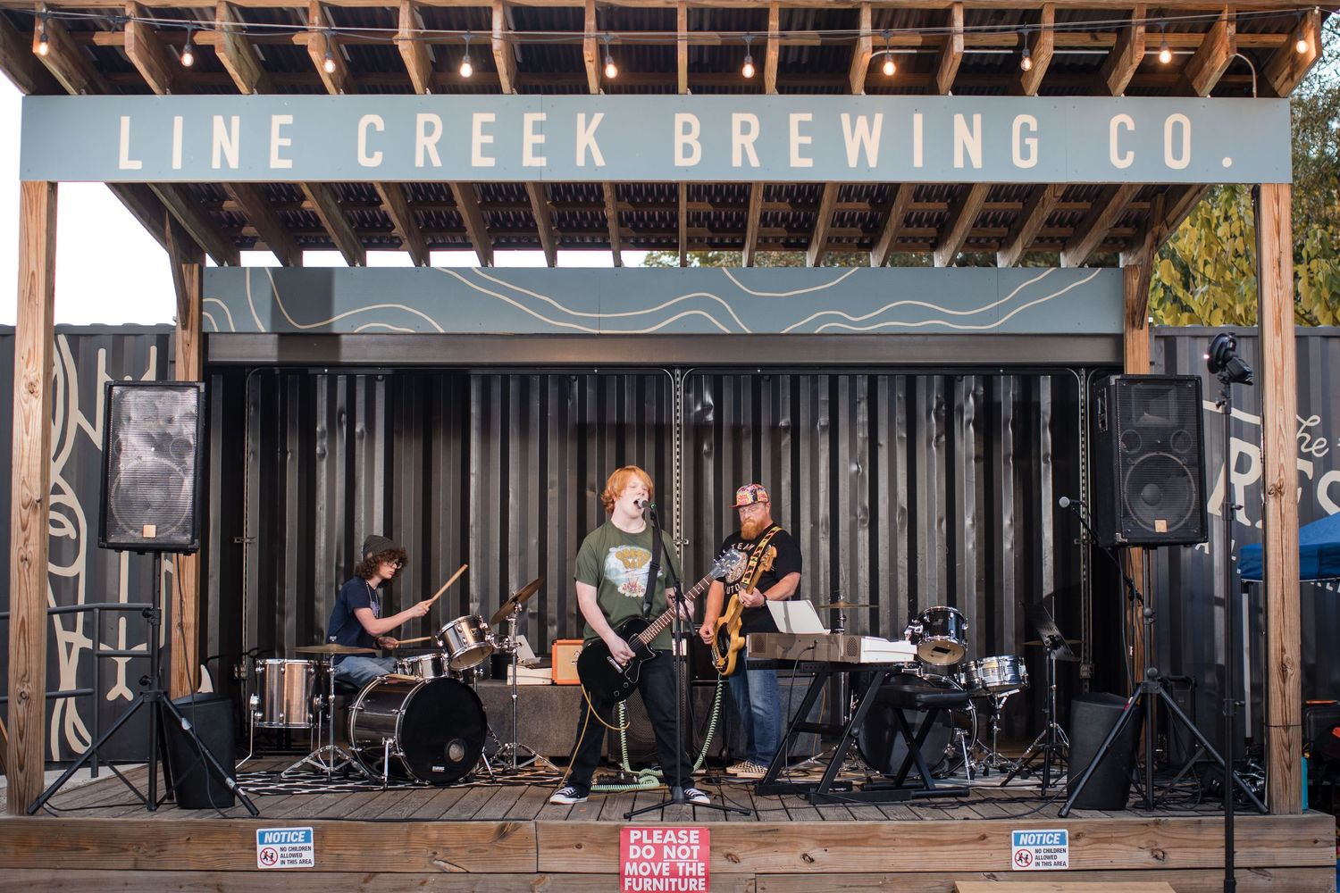 A band performs live music on an outdoor stage at Pine Creek Brewing Co during a sunny afternoon.