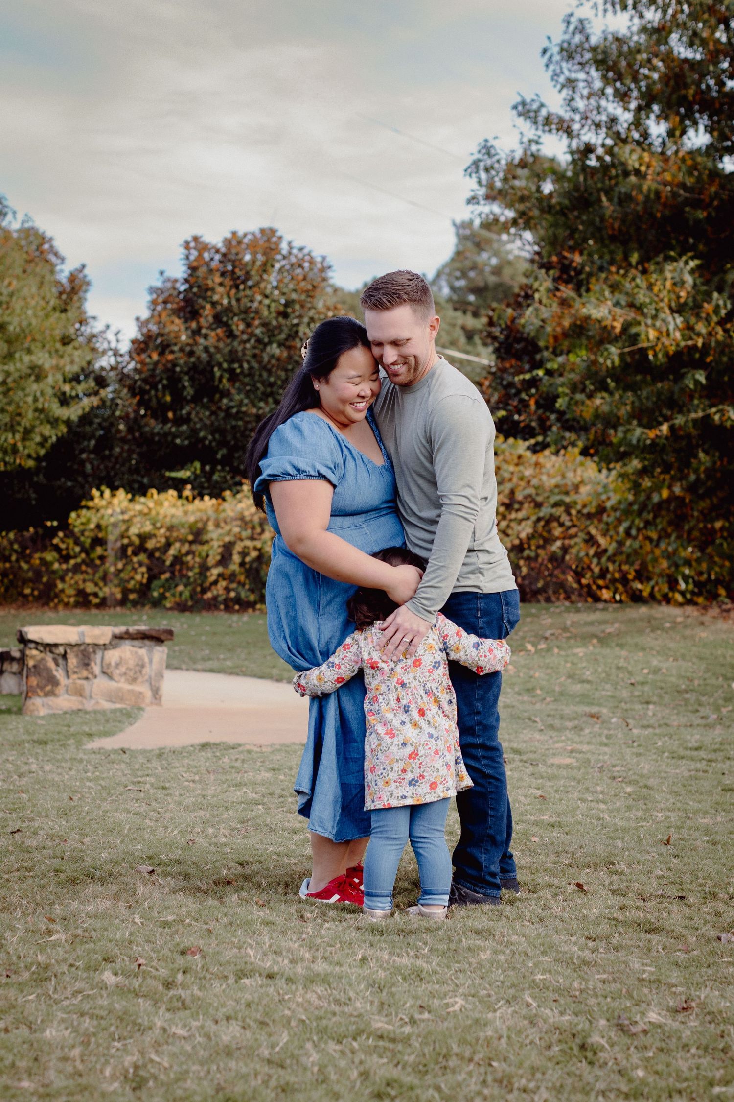 A family shares a tender moment together on grassy terrain during an autumn outdoor photoshoot.