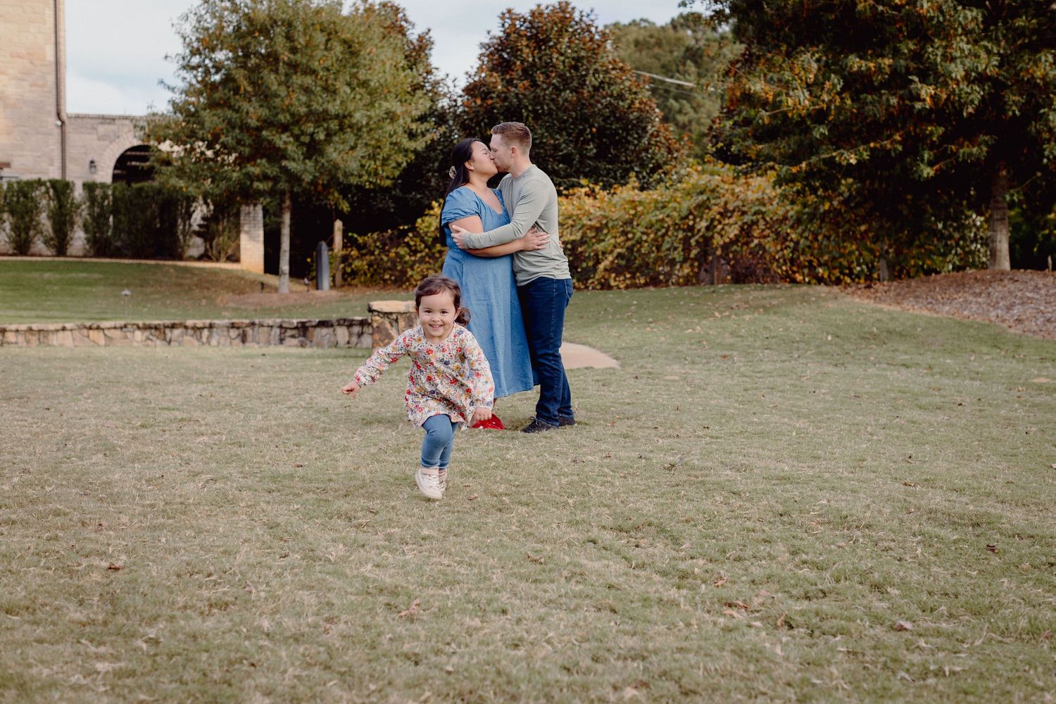 A family plays together on a grassy lawn during an autumn day at a park.