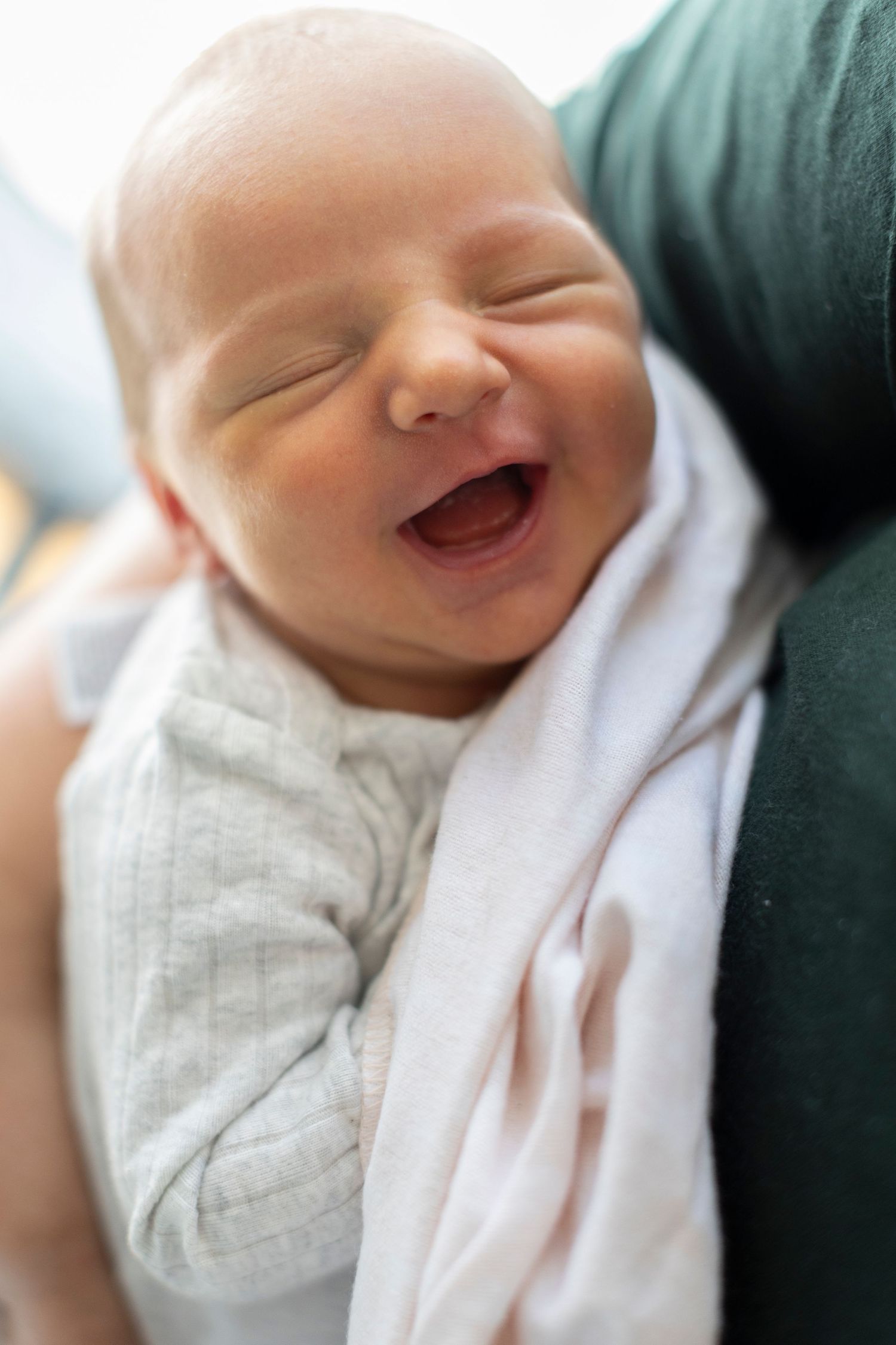 A baby wrapped in white cloth smiles and laughs in a series of close-up photos.