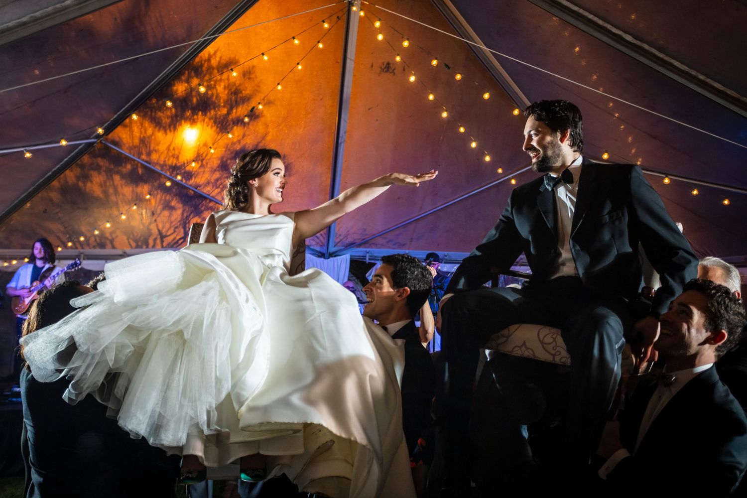Wedding reception dance under a tent with twinkling lights and dramatic orange lighting.