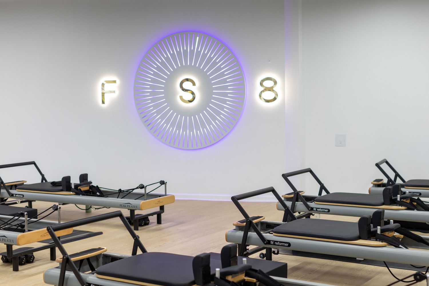 Pilates reformer machines lined up in a modern fitness studio with natural lighting and hardwood floors.