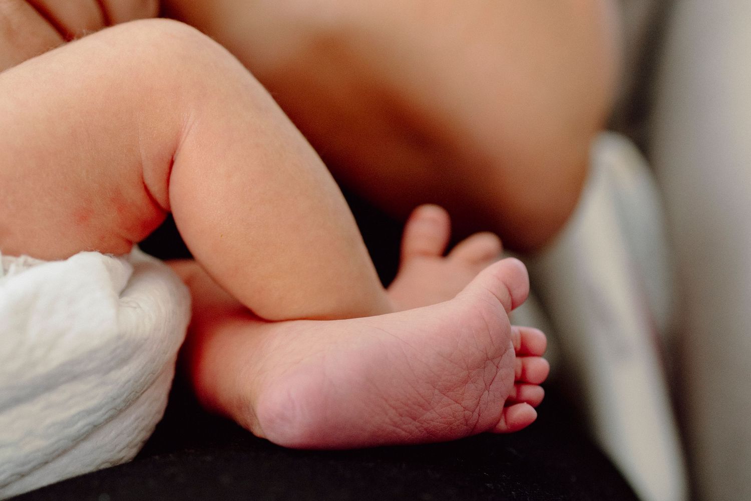 A close-up view of a baby's tiny feet with soft white fabric in the background.