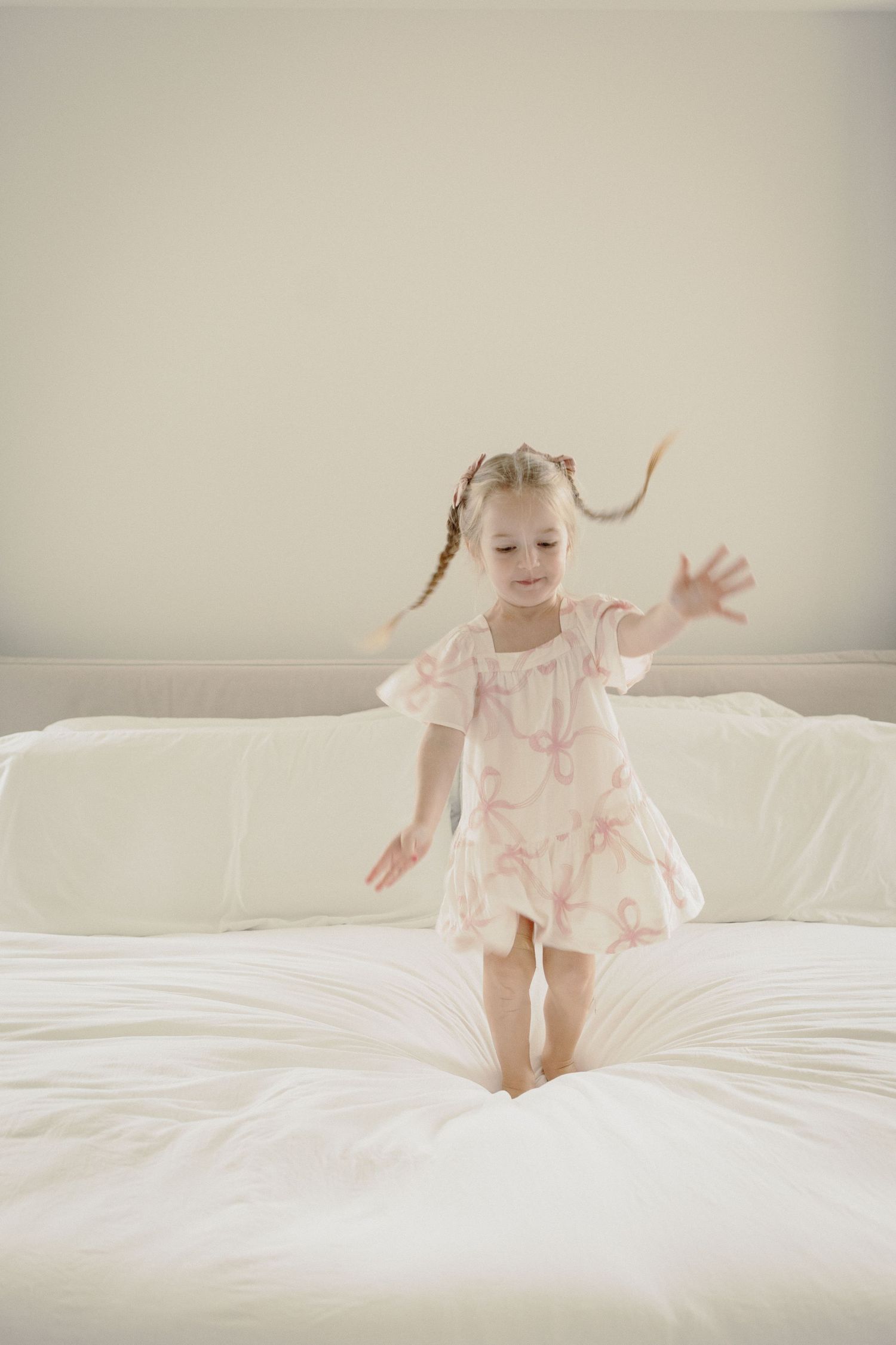 A series of photos showing a child in pink pajamas jumping and playing on a white bed.