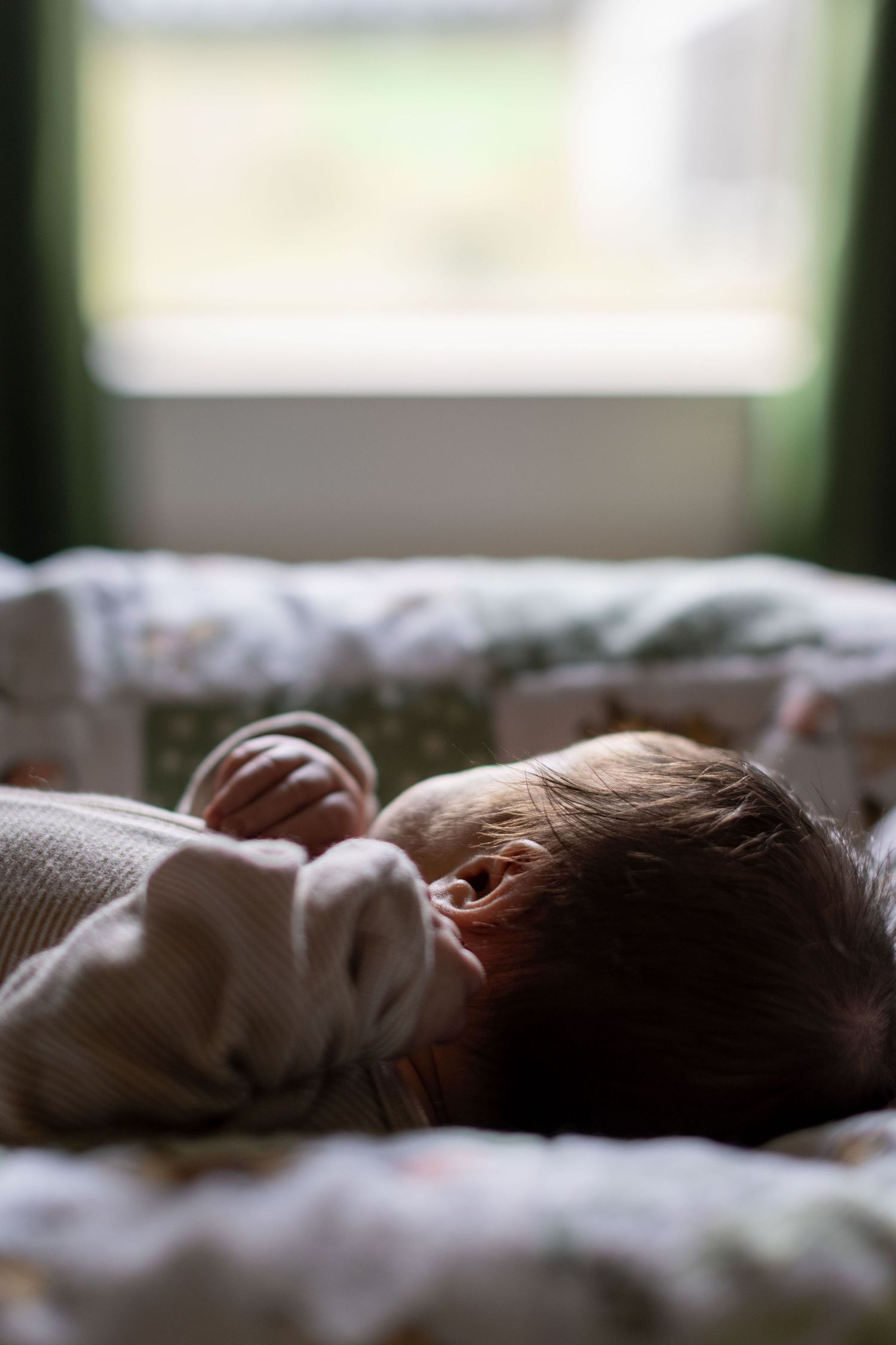 Newborn baby sleeping peacefully on a soft blanket near a window with natural light.
