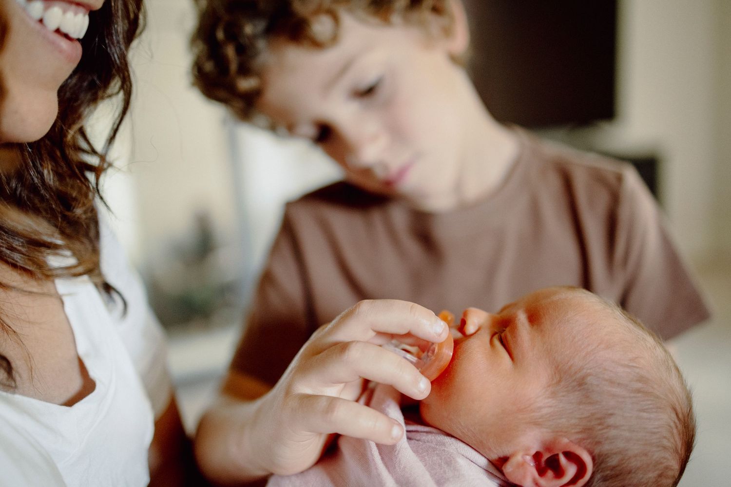 A tender moment as someone gently touches a sleeping newborn baby's face in a soft indoor setting.