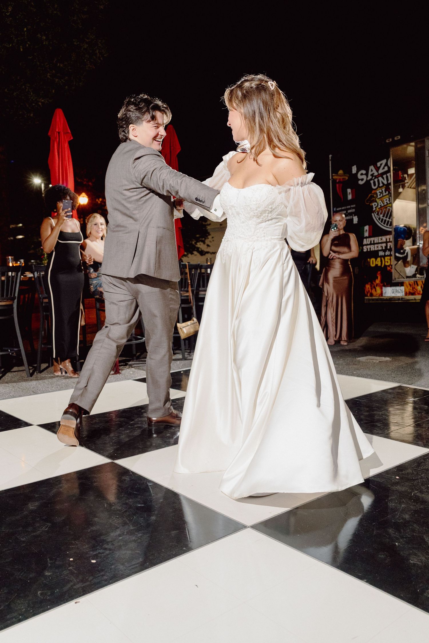 A couple performs a dip during their first dance at a wedding reception on a black dance floor.