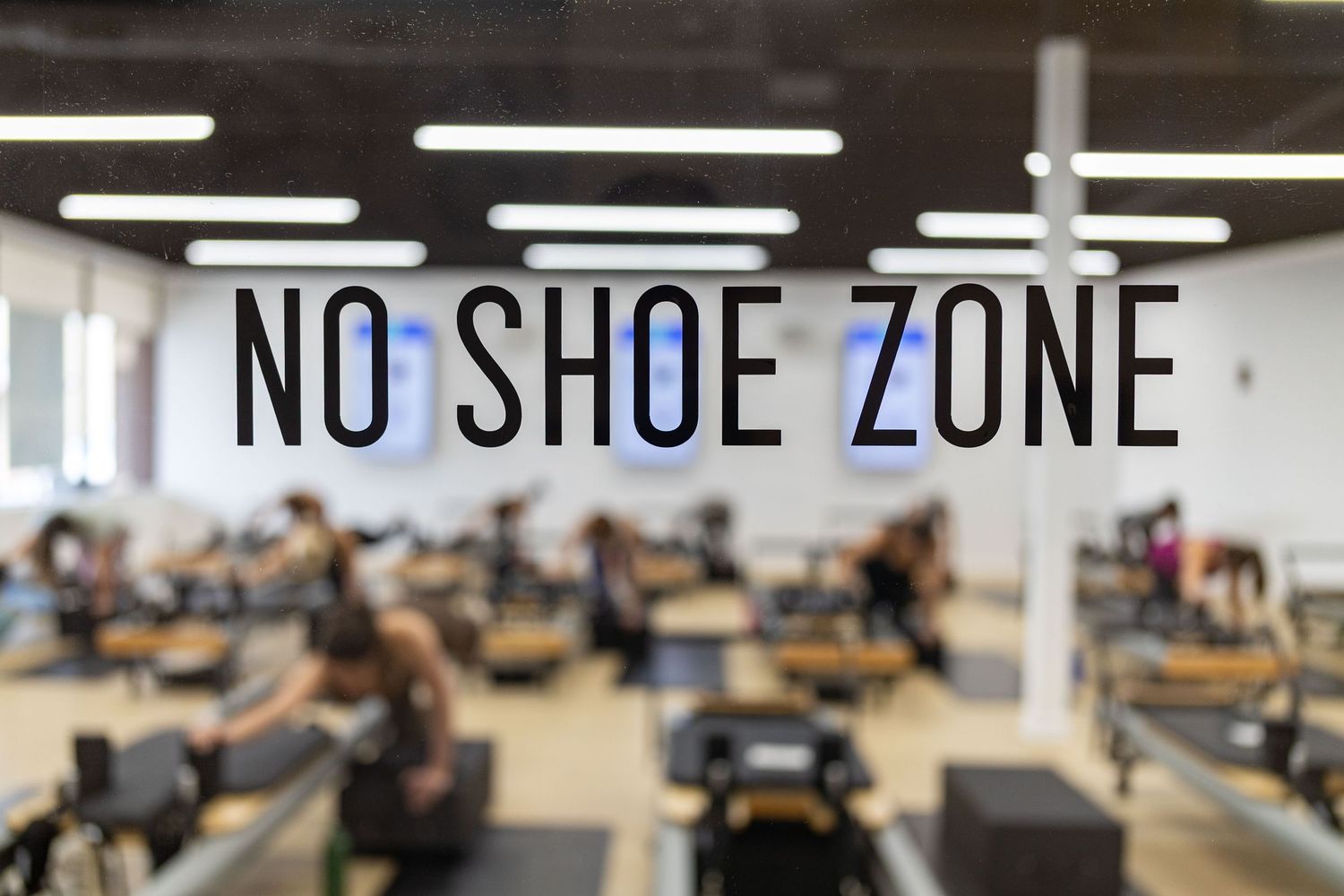 Students work at computer stations in a modern classroom with 'No Shoe Zone' signs visible on the walls.