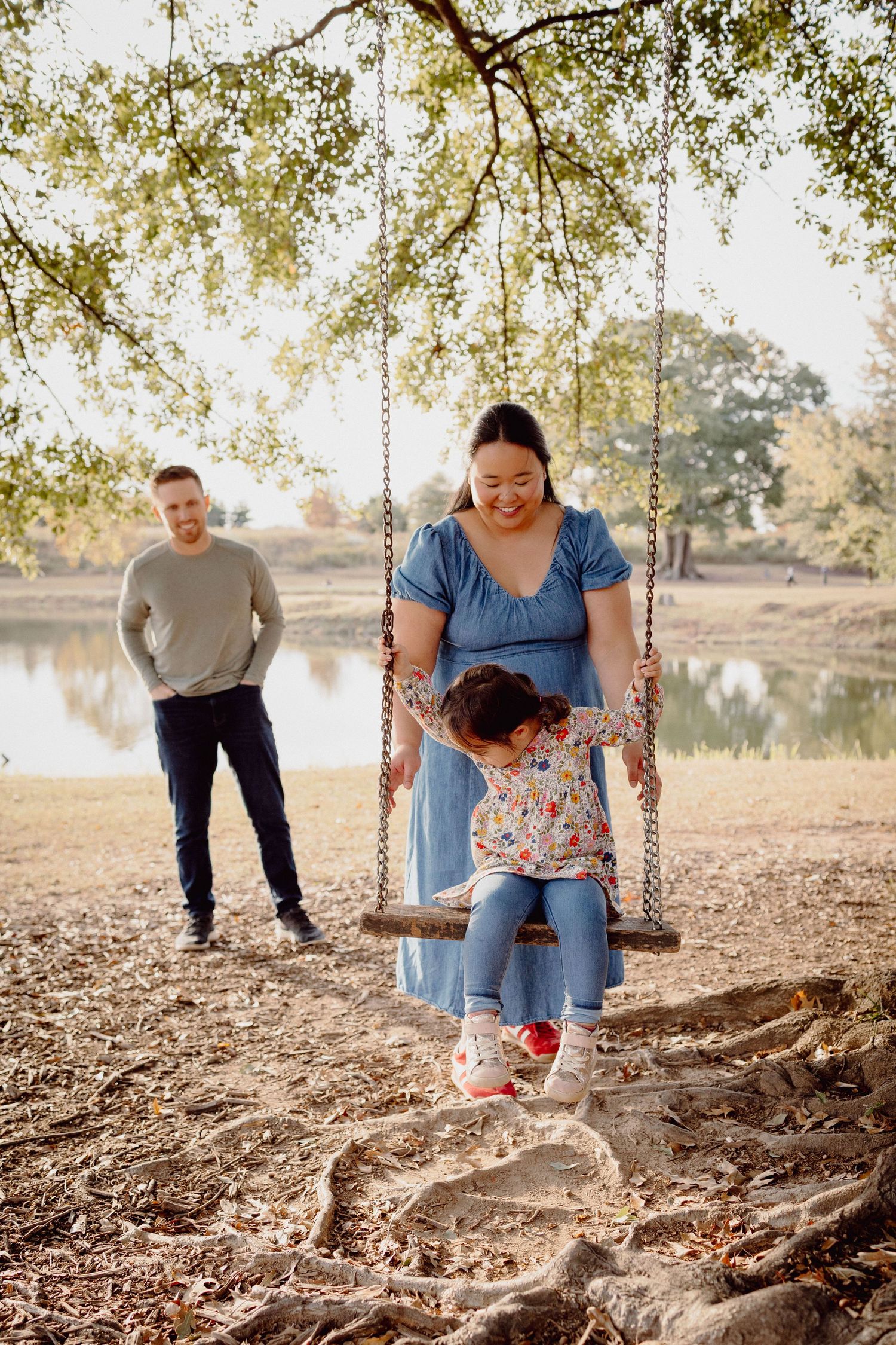 A peaceful family moment by a lake with a rope swing hanging from a tree branch on an autumn afternoon.