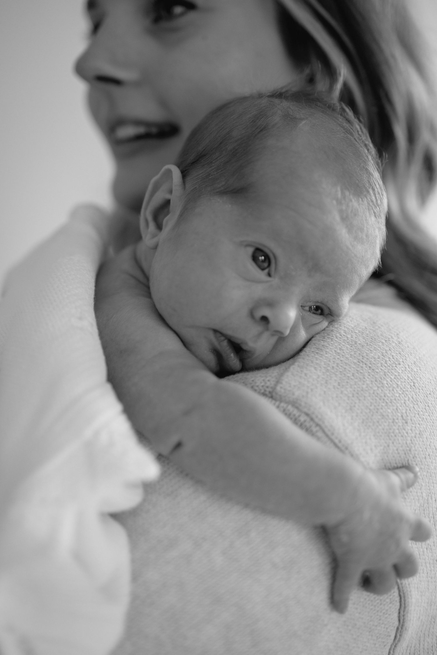 A series of black and white photos showing a newborn baby swaddled in soft white blankets.