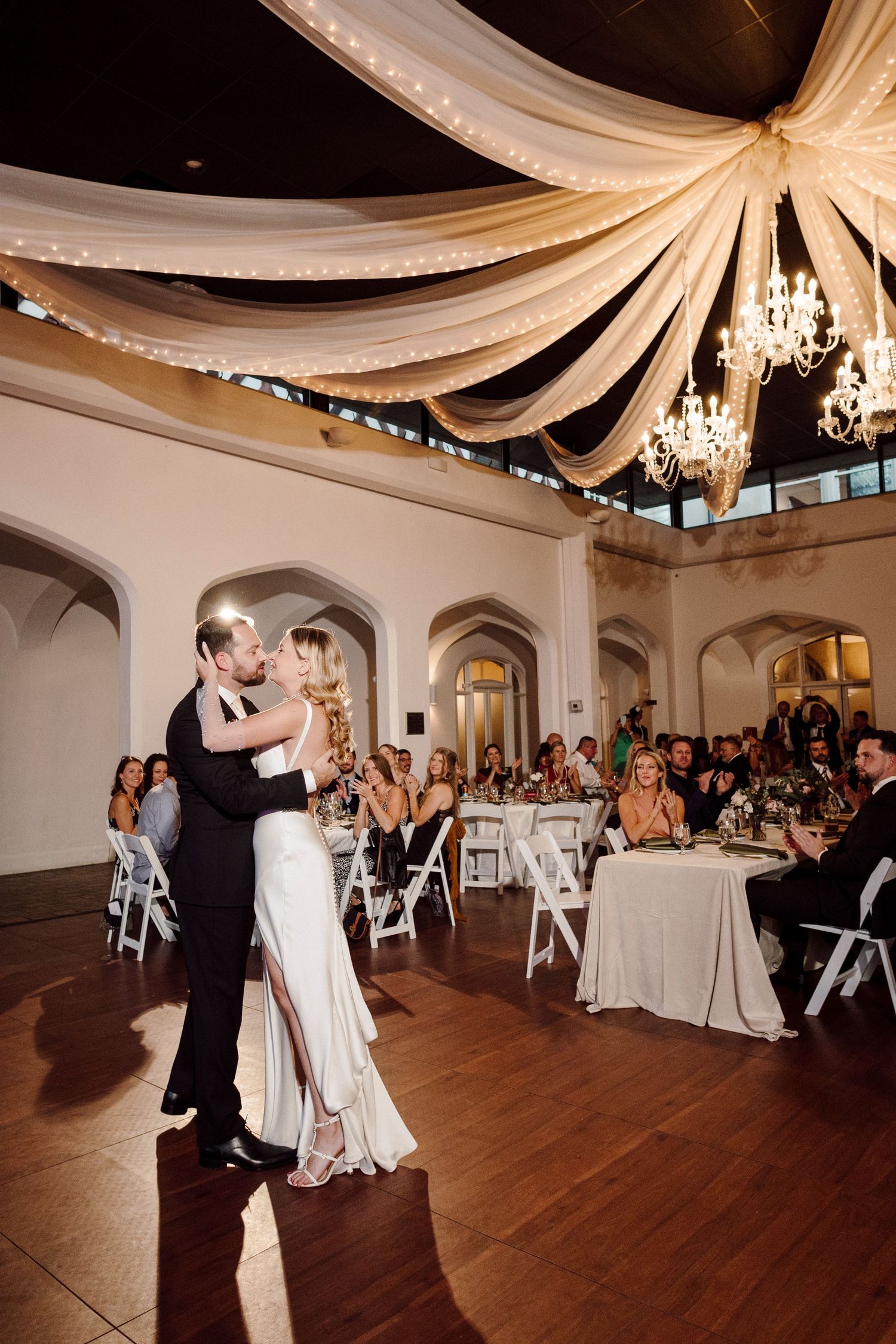 Wedding reception dance floor with elegant white draped ceiling and crystal chandeliers.