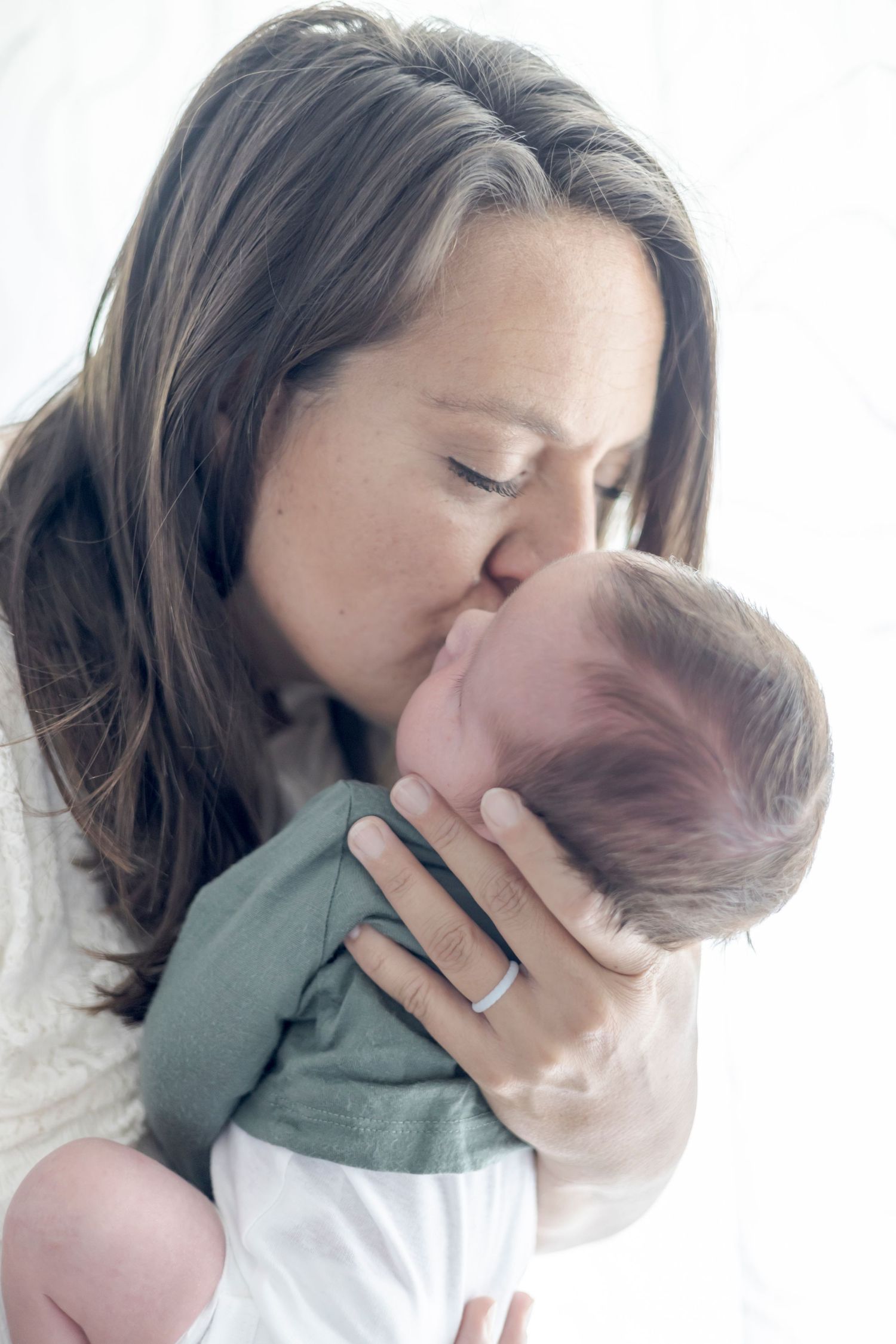 A loving mother gently kisses her newborn baby on the forehead while cradling the infant in her arms.