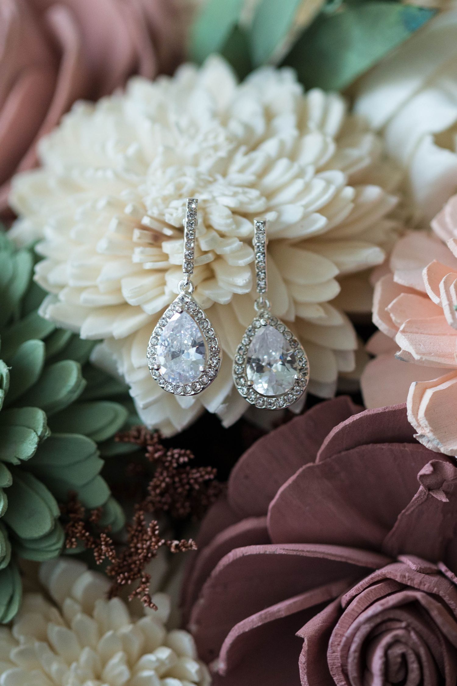 Sparkling crystal teardrop earrings displayed among white and burgundy wedding flowers.