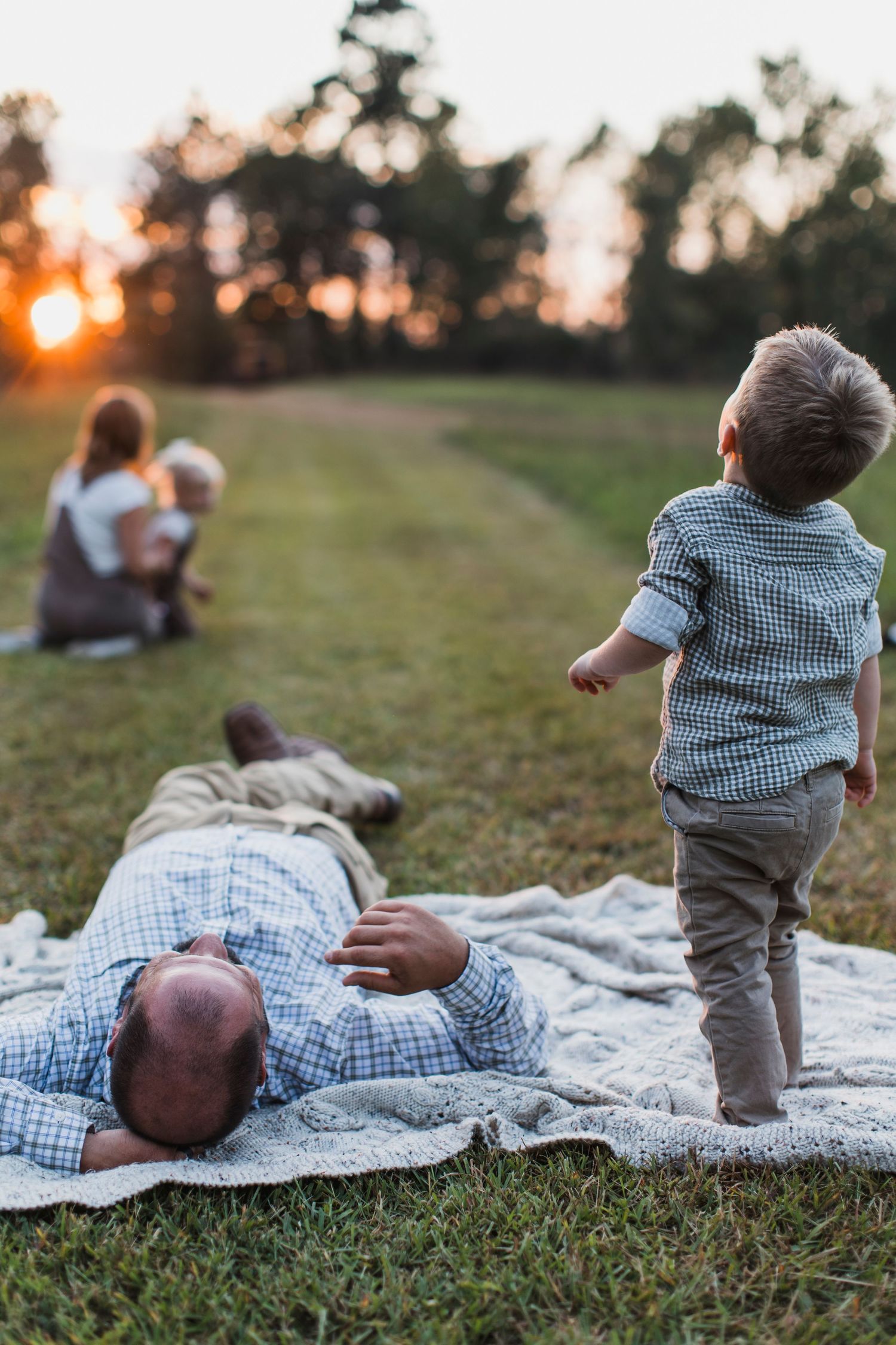 Series of images showing a baby rolling and playing on a white blanket in the grass during golden hour.