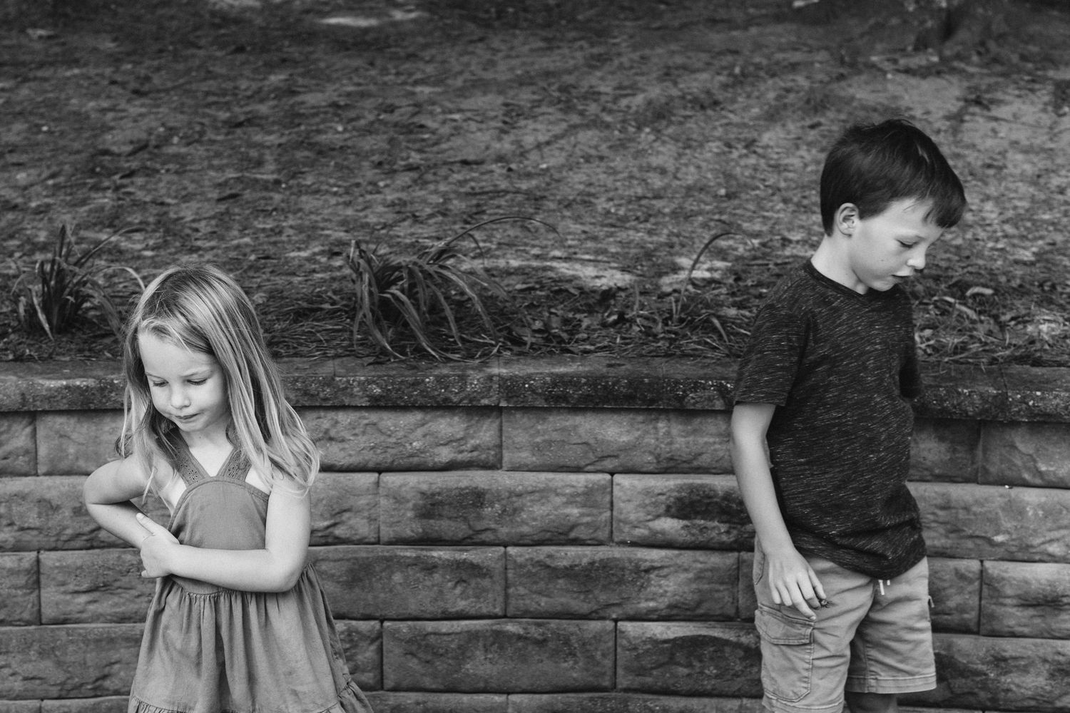 Children play and interact together on a stone wall in a park setting during an outdoor activity.
