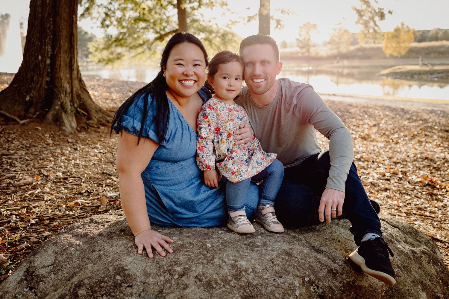 A family enjoys a warm autumn day together sitting on fallen leaves in a park during golden hour.