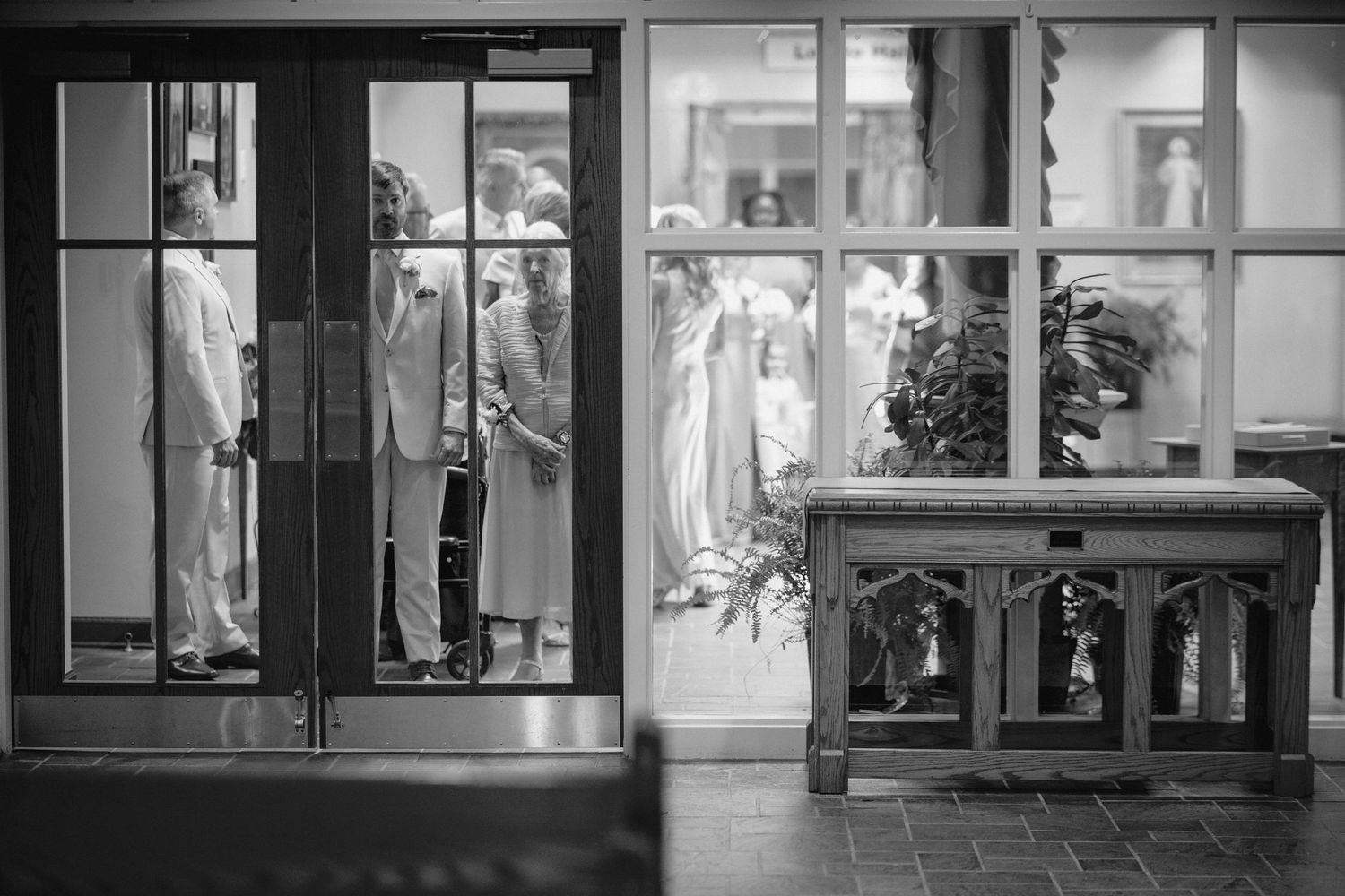 Black and white photo of elegantly dressed guests entering a venue through glass doors at a formal event.