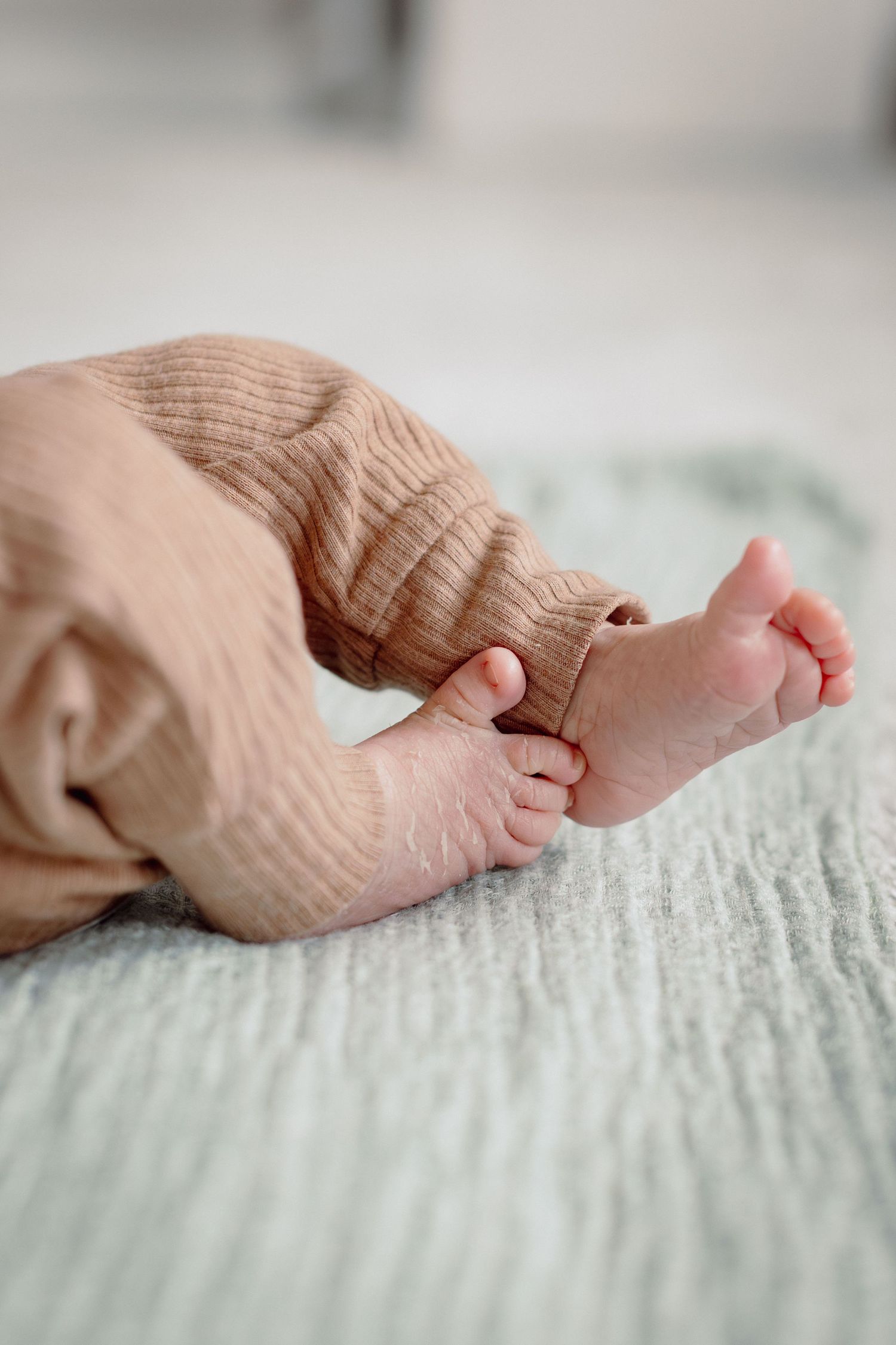 Close-up of tiny newborn baby feet in a soft pink ribbed onesie resting on a light blue blanket.