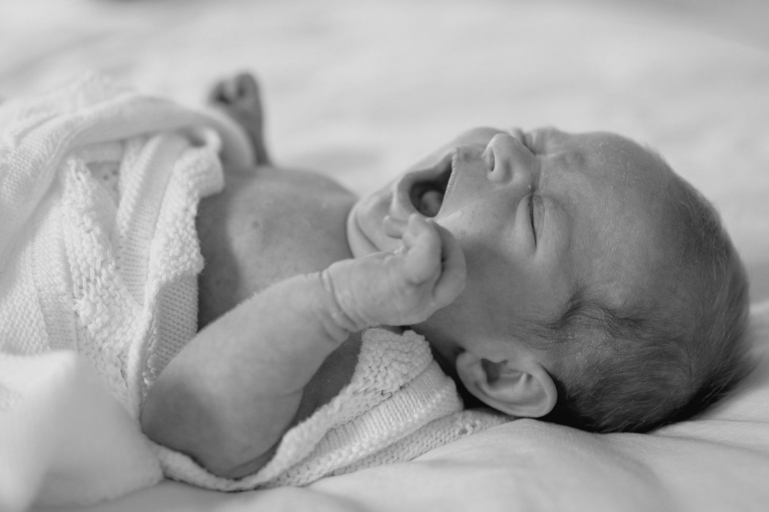 A series of black and white photographs showing a sleeping baby in different poses on white bedding.