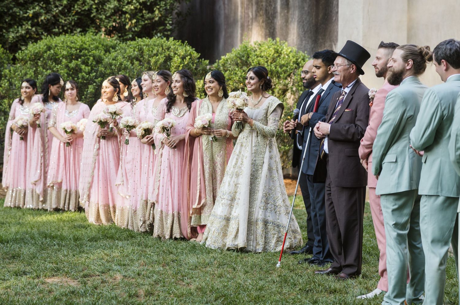 Large wedding party lined up outdoors wearing pink and neutral colored attire.