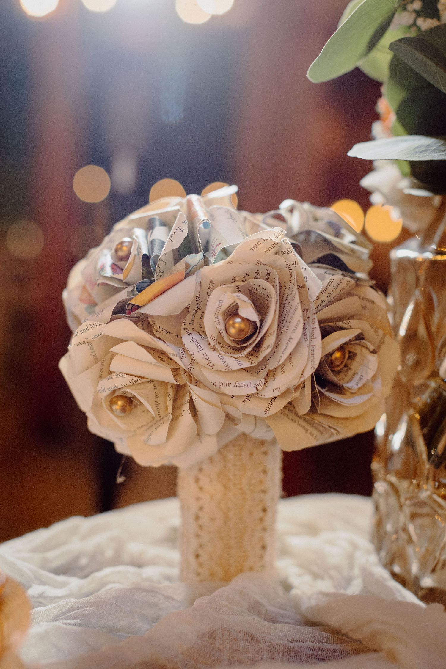 Handmade paper roses in soft beige tones arranged in vintage hobnail vases with romantic bokeh lighting in background.