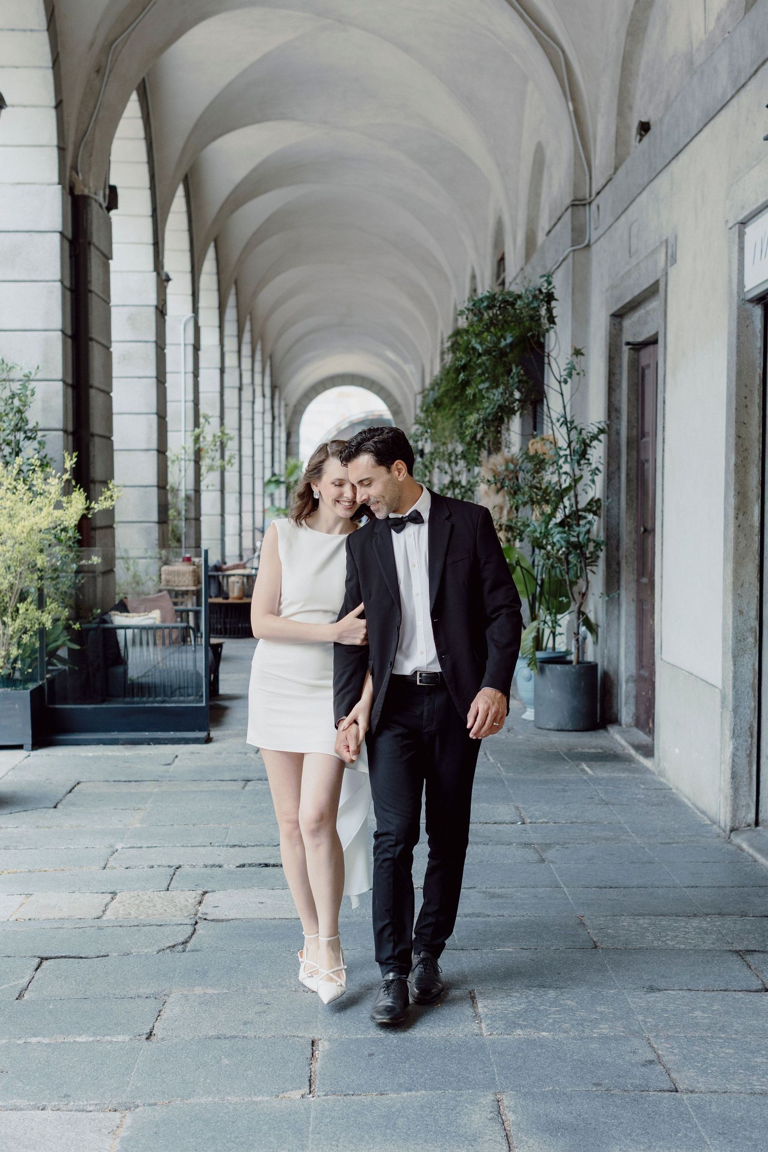 Couple walking intimately under elegant stone archways.