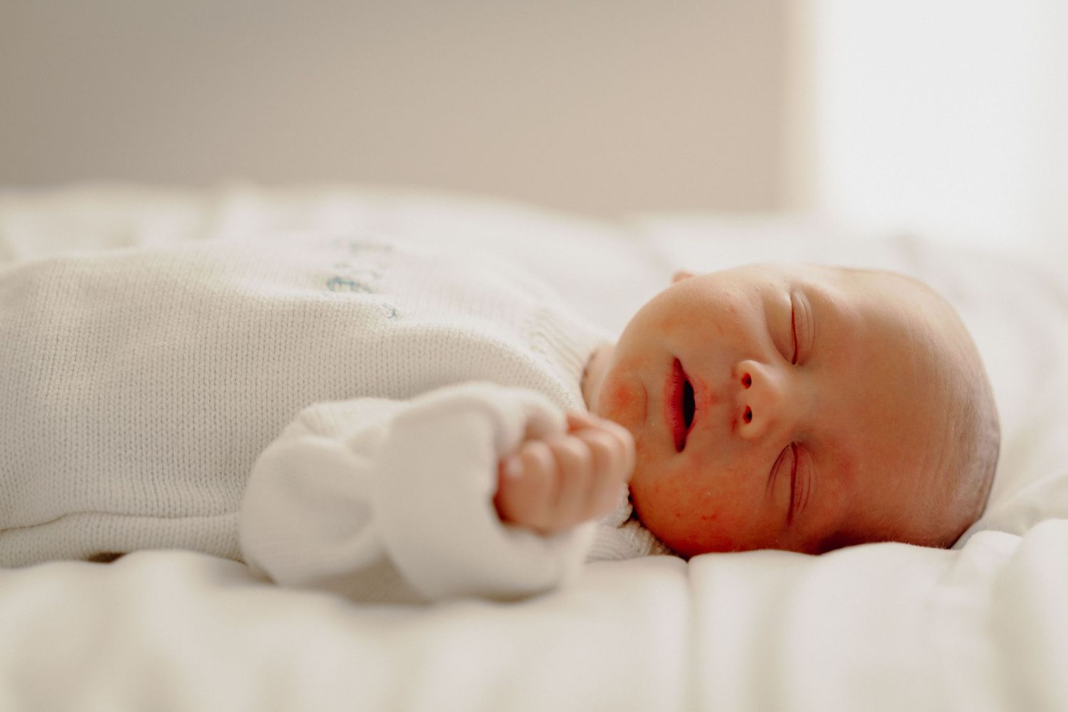 Newborn baby sleeping peacefully on soft white bedding in natural light.