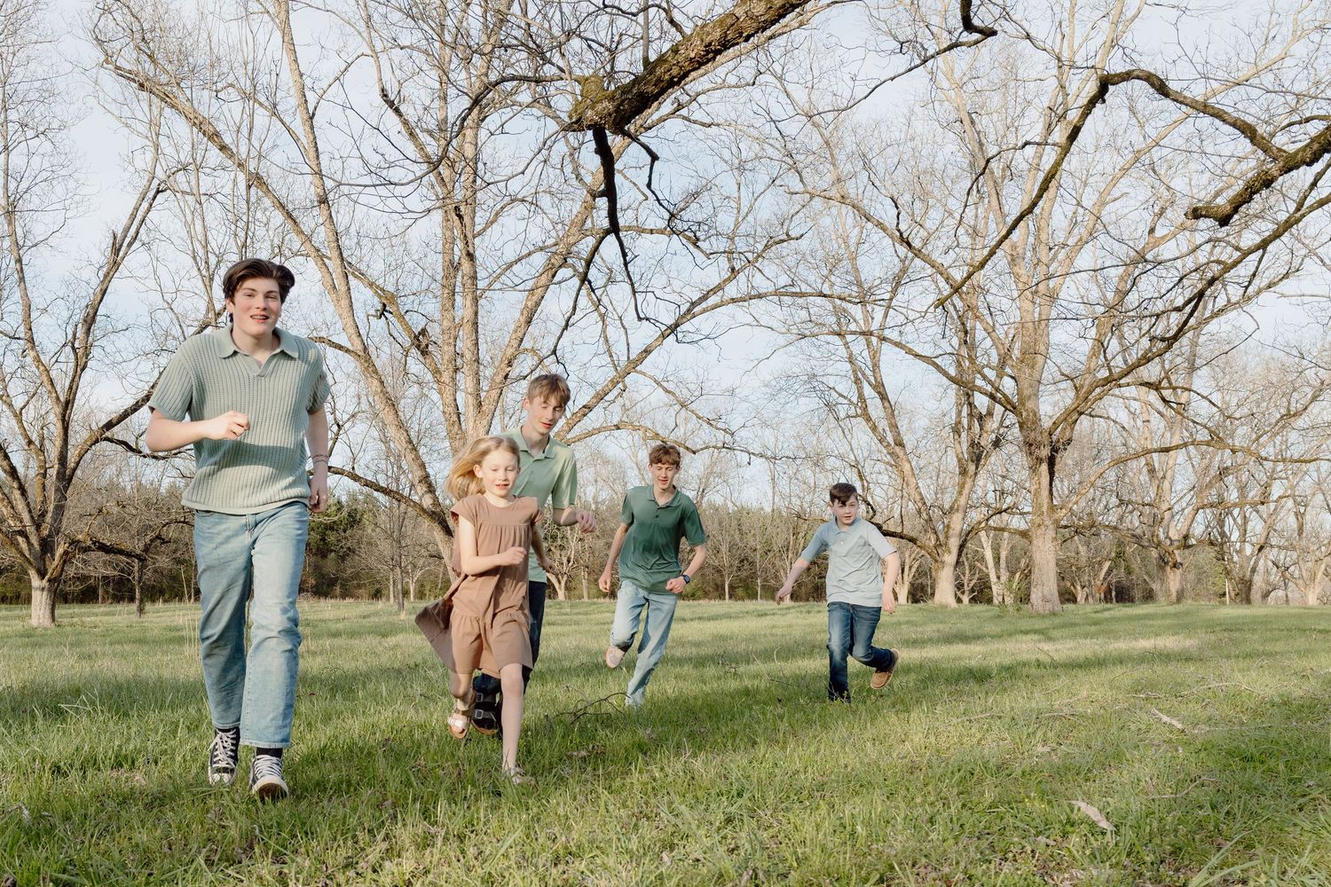 Children run and play together on a grassy hillside during a sunny spring day.