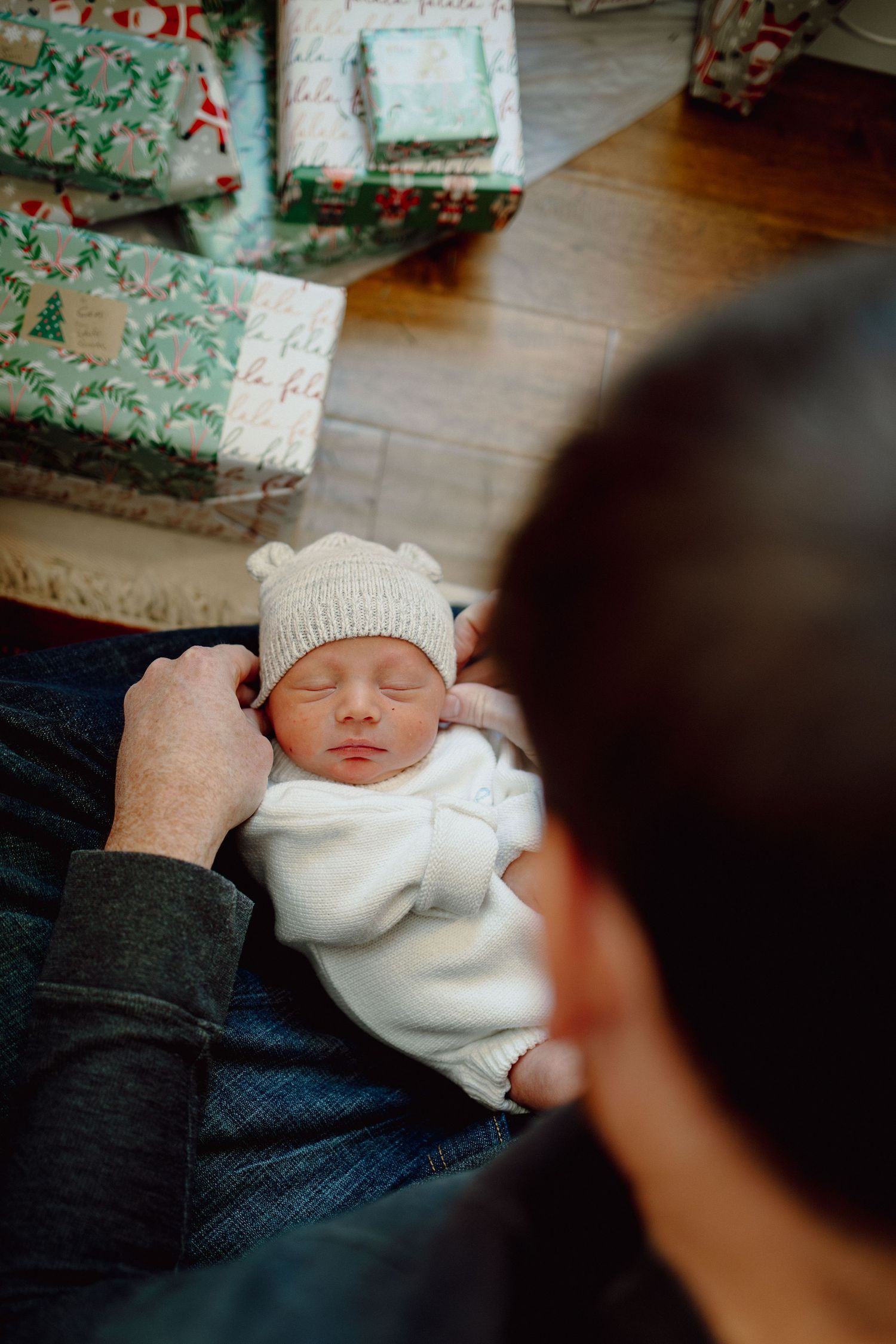 A sleeping newborn baby wearing a white knit hat and swaddled in white fabric rests peacefully.