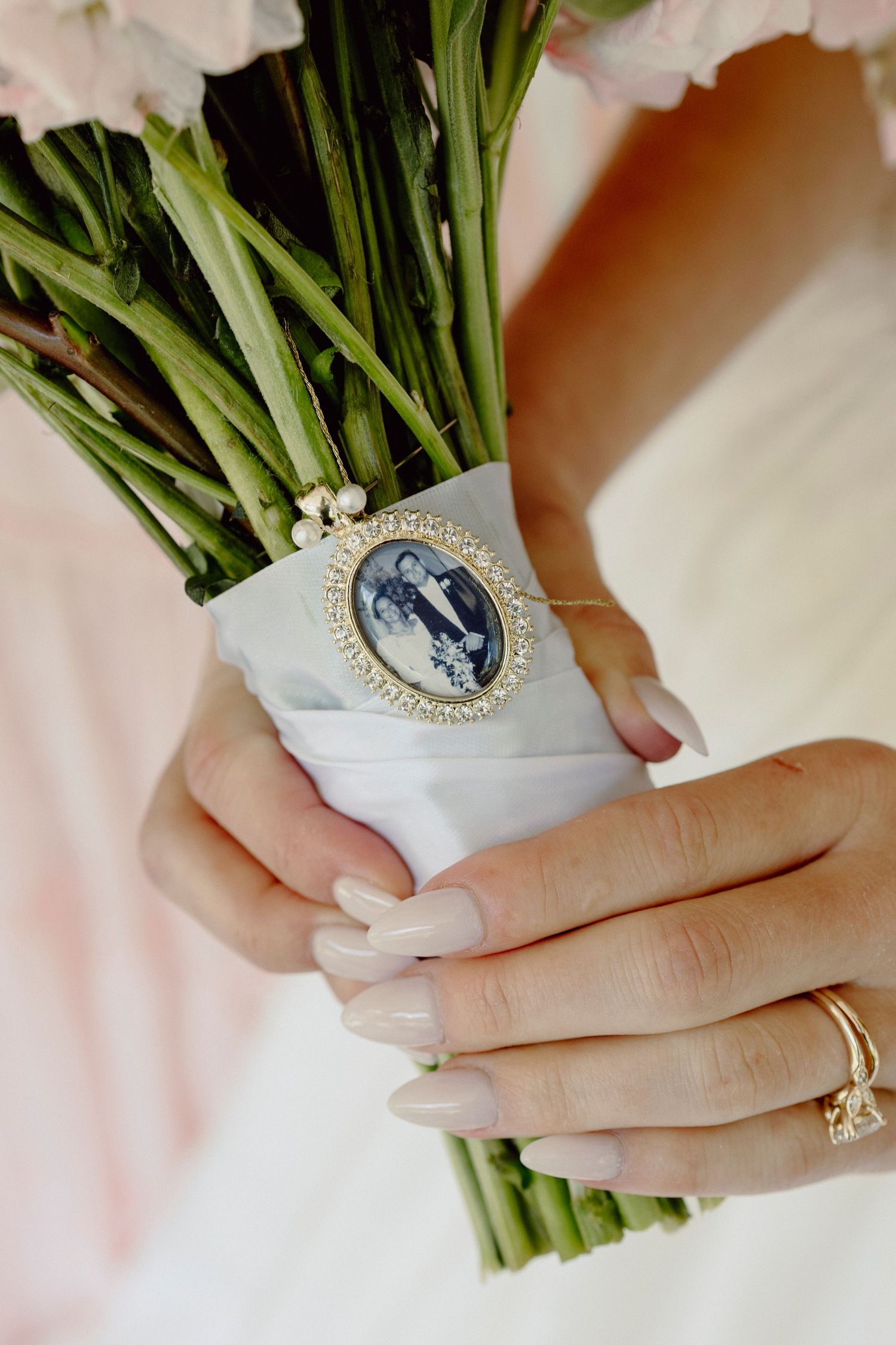 Close-up of bridal bouquet stems wrapped in white fabric with vintage brooch detail.