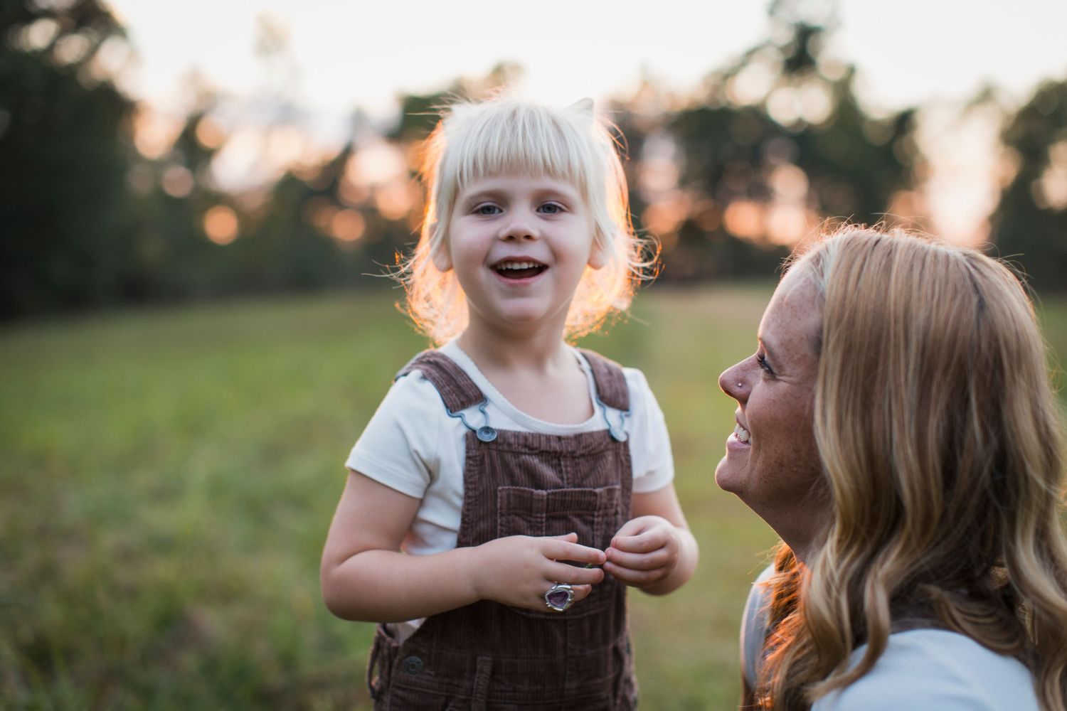 A candid family moment captured at sunset in a grassy field with warm golden lighting and natural expressions.