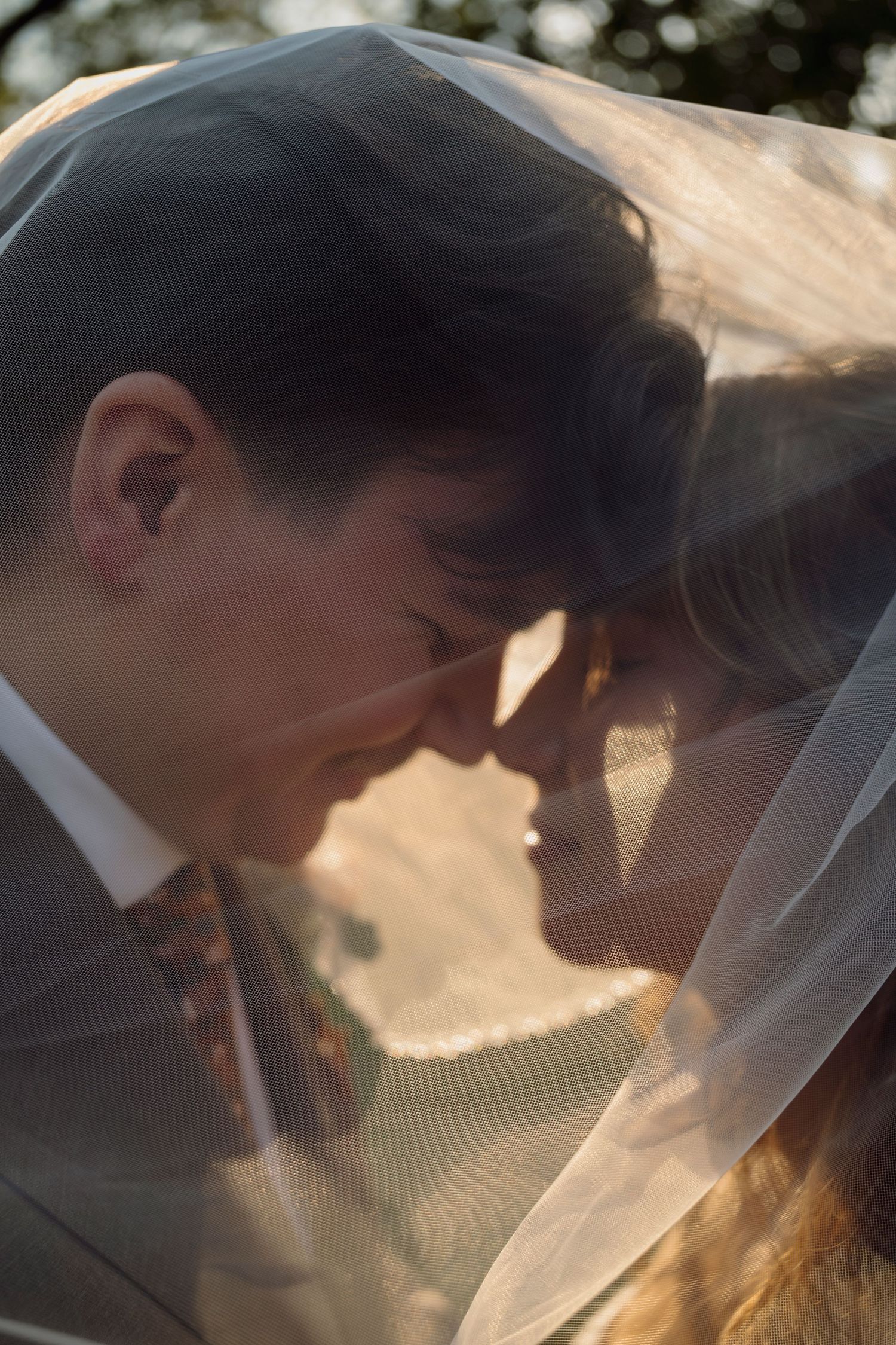A romantic silhouette of a couple sharing a tender moment under a veil during sunset.