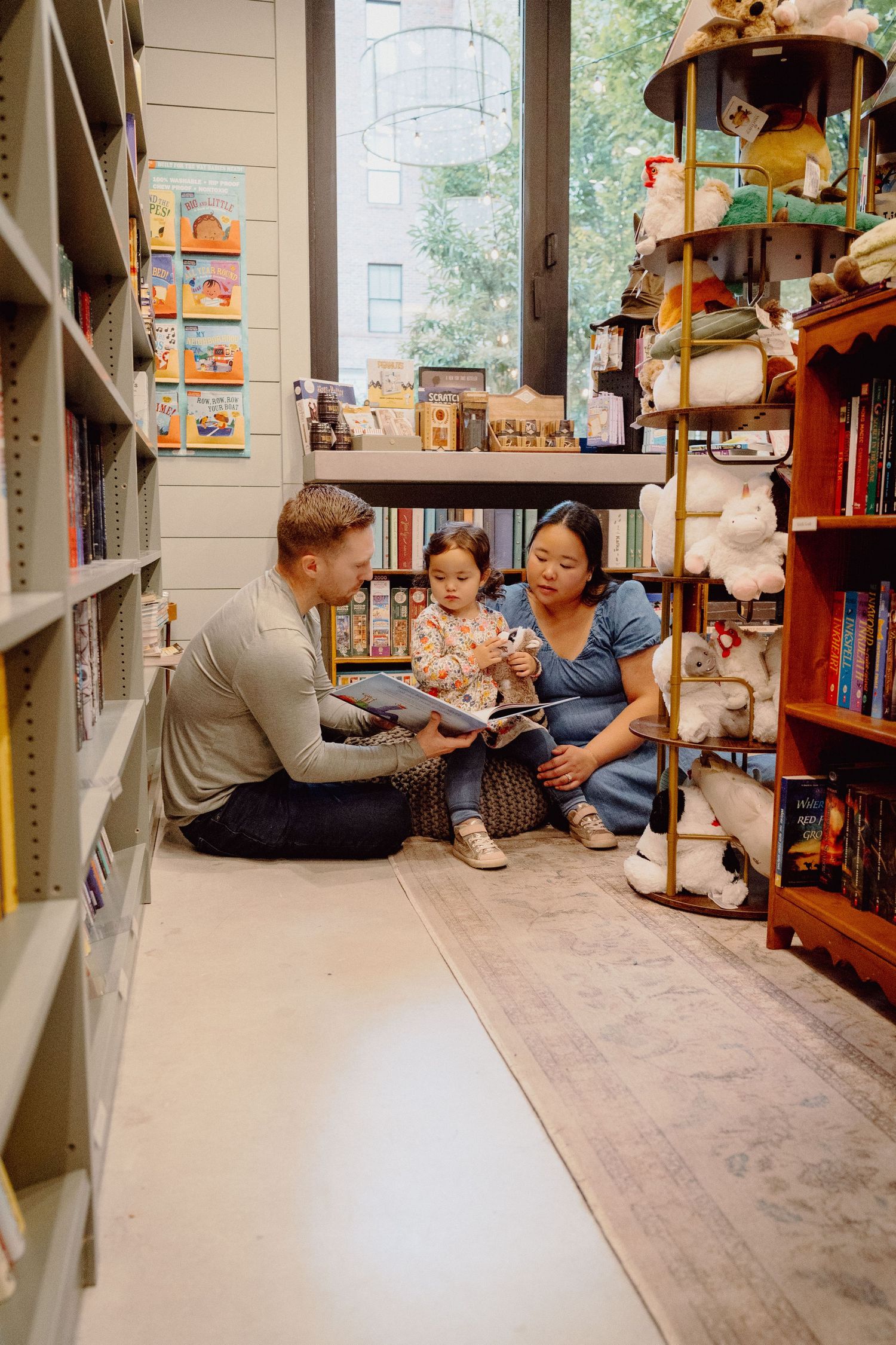 Family browses books together in a cozy bookstore with wooden floors and shelves filled with children's literature.