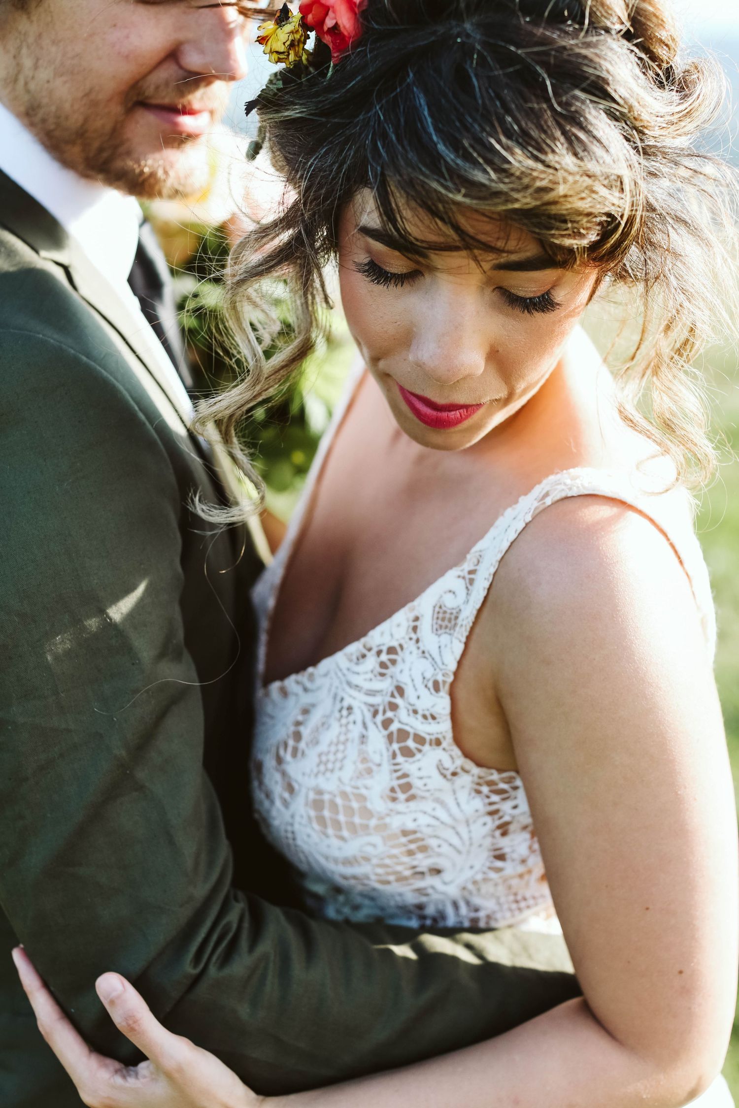 Romantic wedding couple embraces in delicate white lace dress and dark suit outdoors.