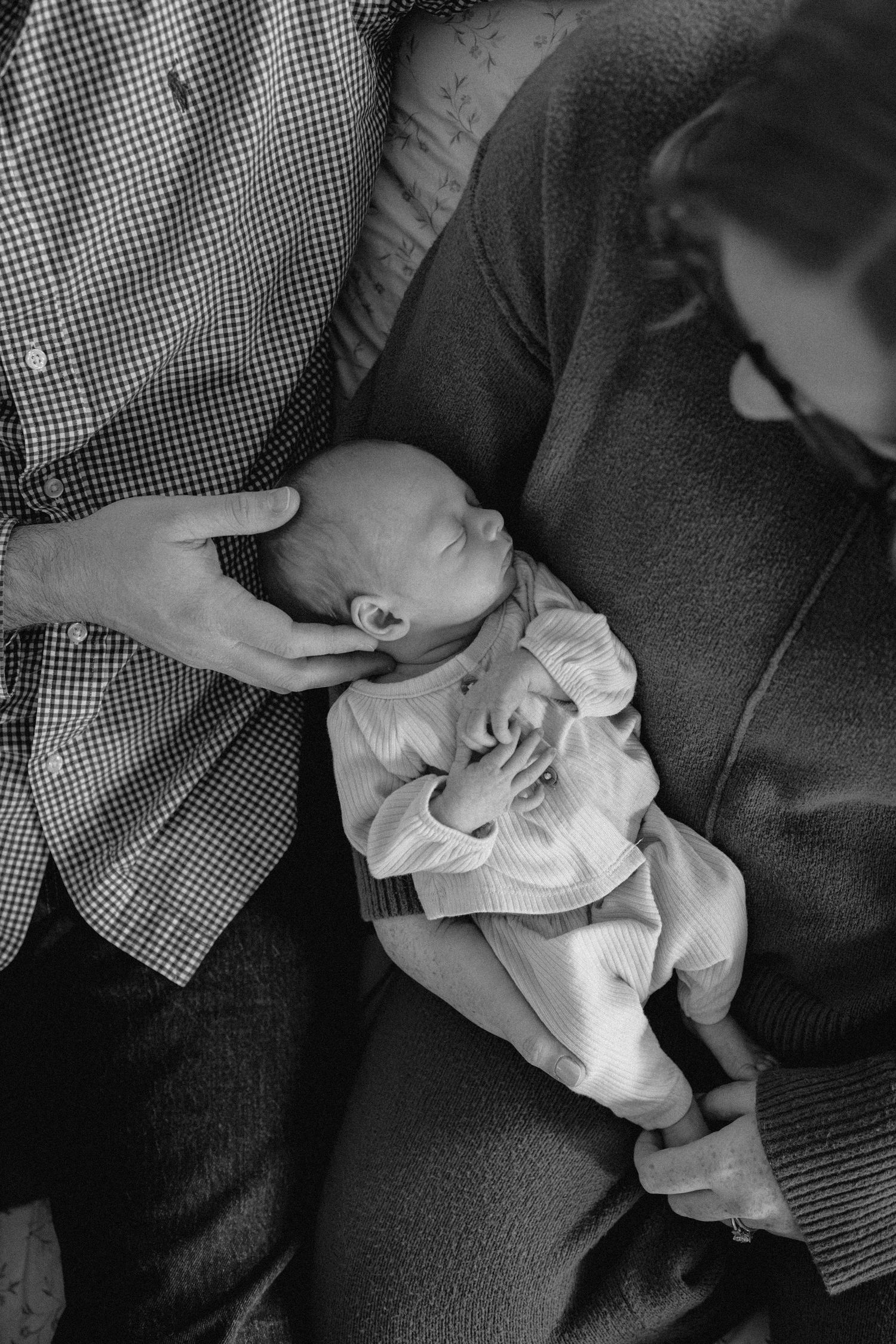 Black and white photo series showing someone cradling a sleeping baby in white clothing on their lap.