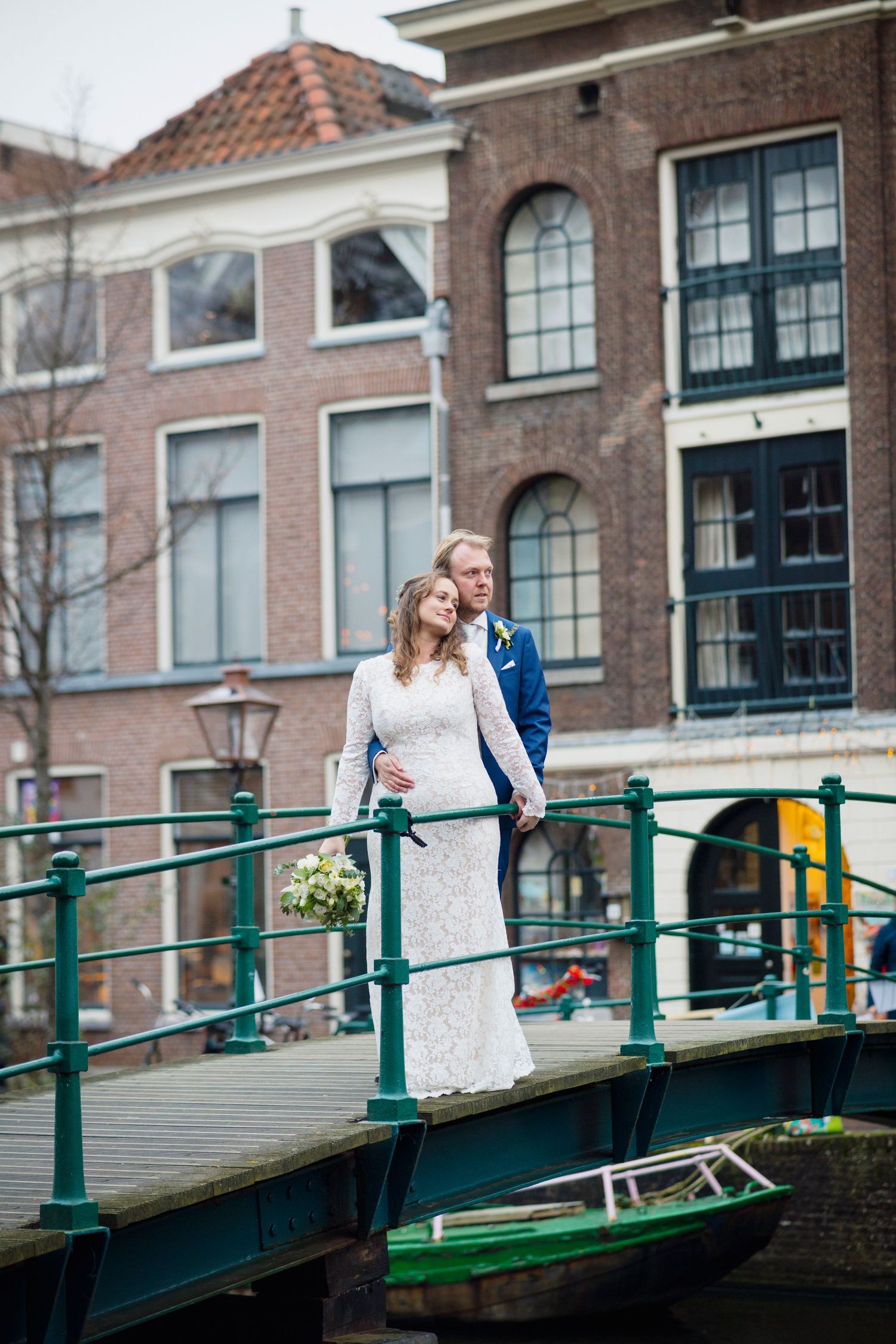 Couple posing on historic bridge with green railings in European city setting.