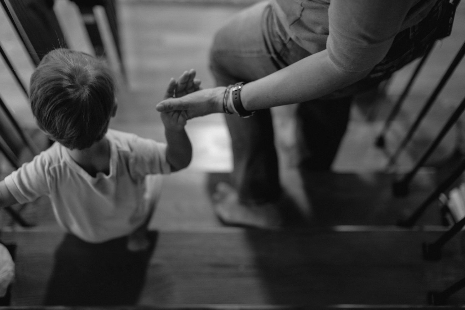 Black and white photo of adult holding child's hand on stairs, guiding them up steps.