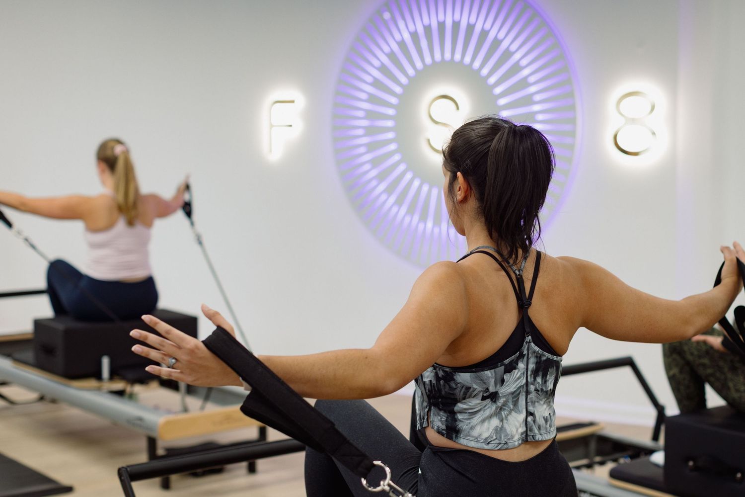 Person exercising on a Pilates reformer machine with resistance springs in a bright studio setting.