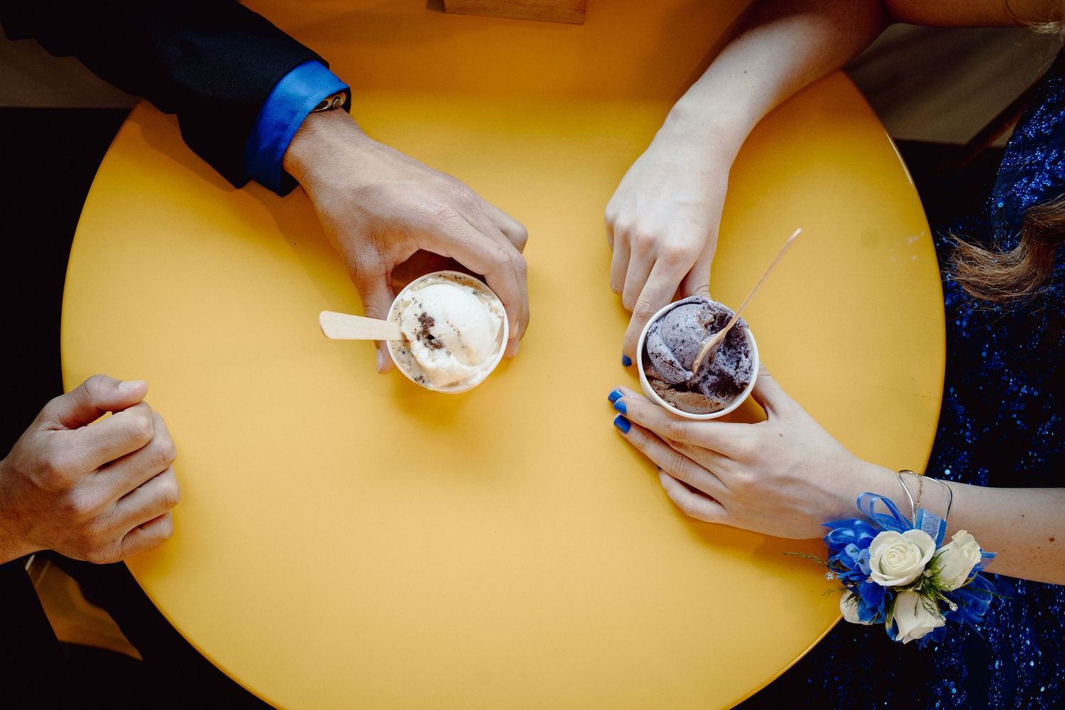 Two people sharing ice cream drinks at a yellow table, one wearing a blue corsage and blue dress.