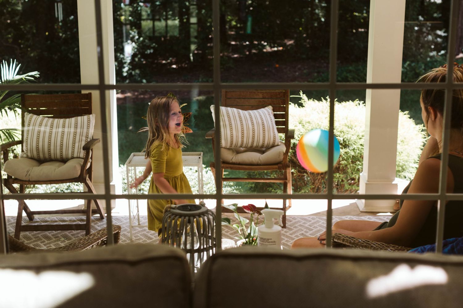 A row of porch rocking chairs with striped cushions overlook a peaceful garden setting at sunset.